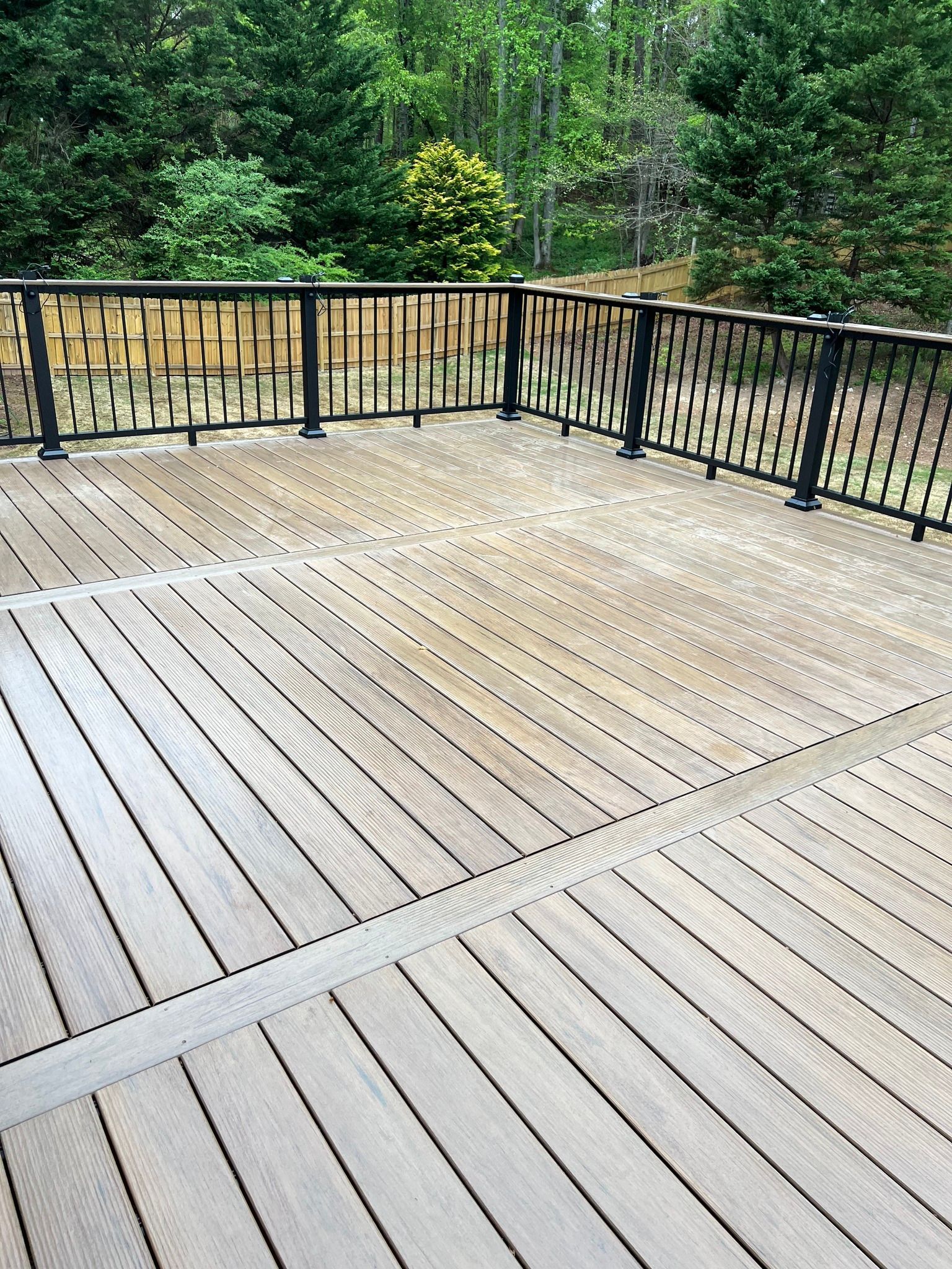 Wooden deck with black railing overlooking a green yard.