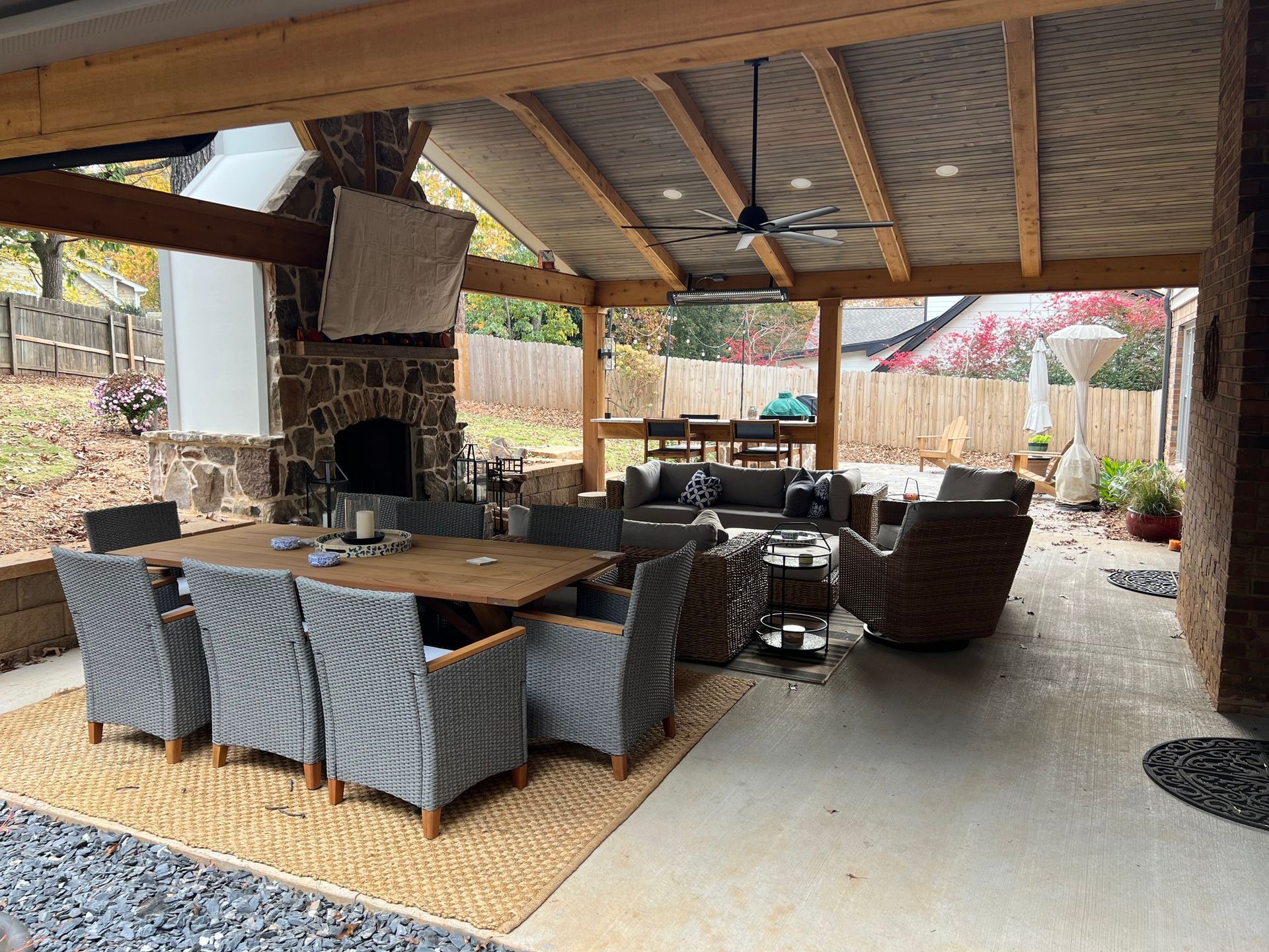Covered outdoor patio with dining and living areas; fireplace, ceiling fan, and backyard view.