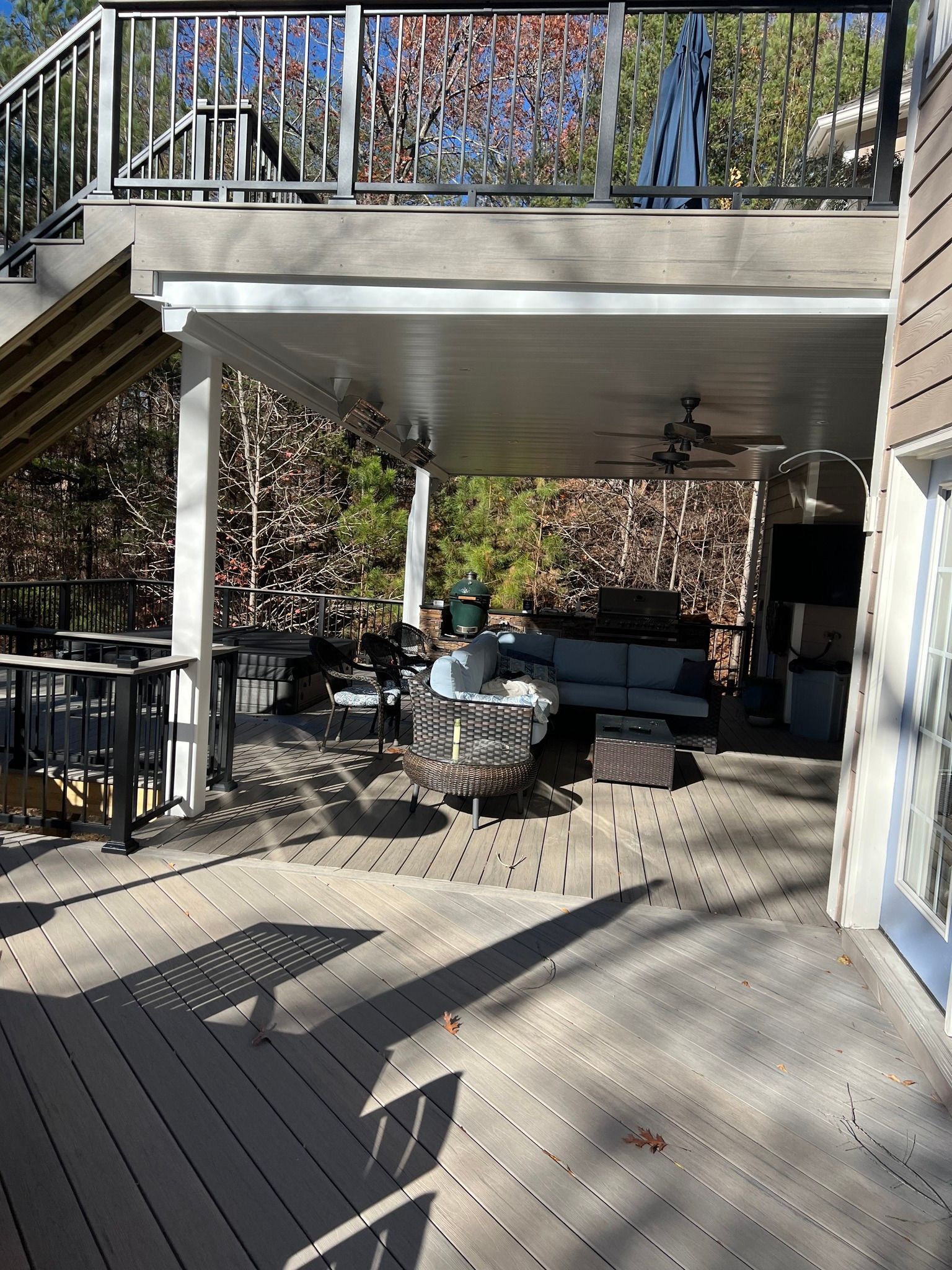 Outdoor deck with seating under a covered area and a deck above, surrounded by trees.