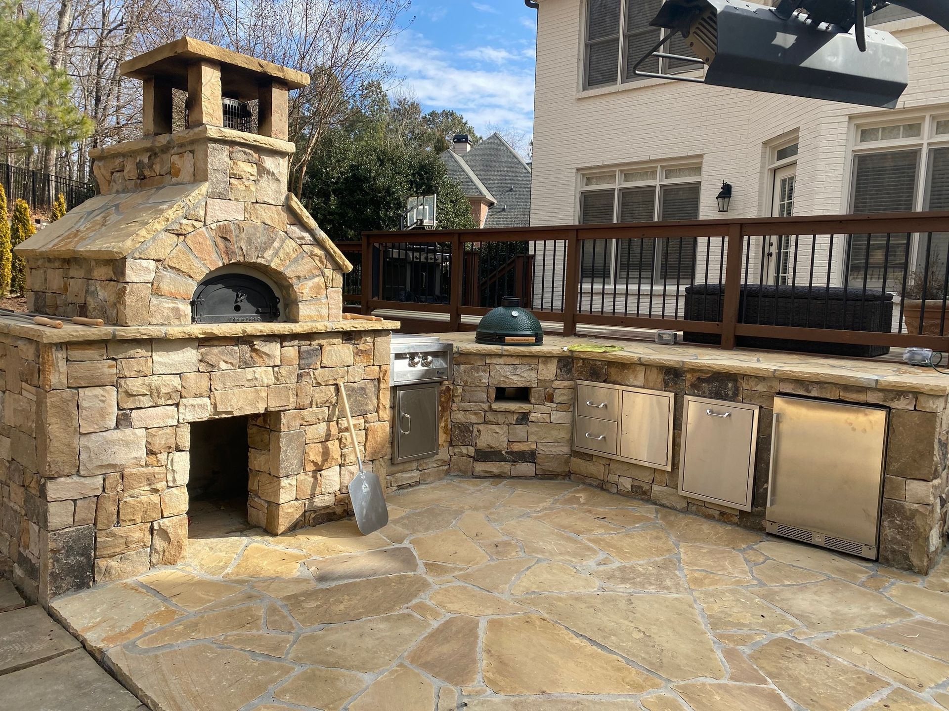 Outdoor stone kitchen with pizza oven and built-in appliances on a flagstone patio.