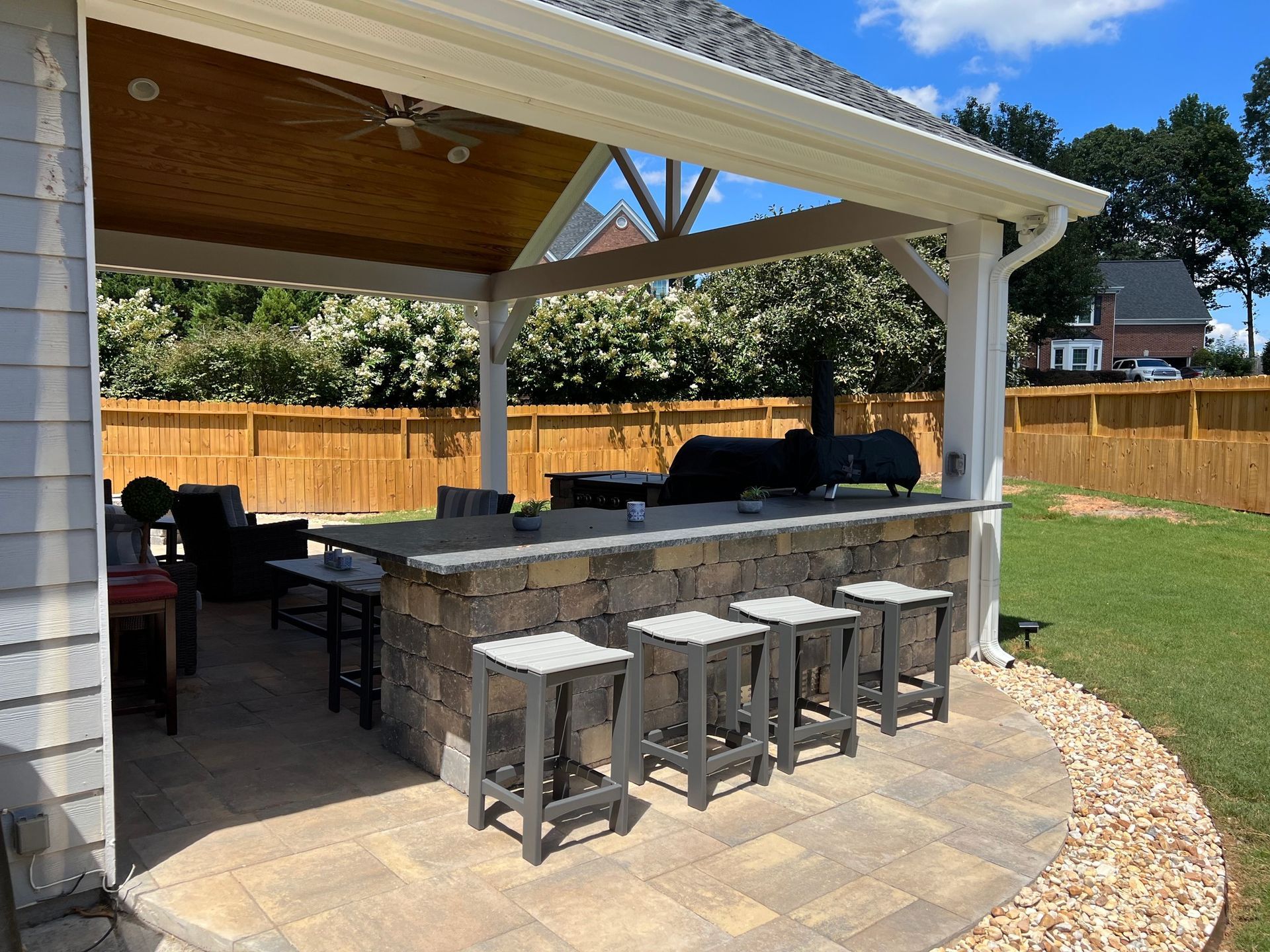 Outdoor kitchen with bar seating, smoker, and seating area under a covered patio with a backyard.