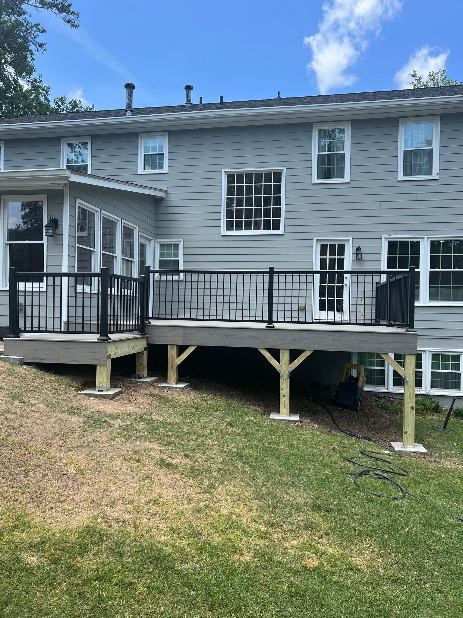 Deck with black railing, gray siding house, and green lawn.