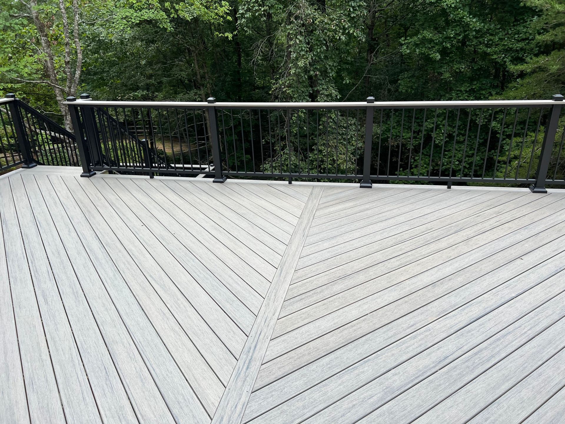 Gray composite deck with black railing overlooking a wooded area.