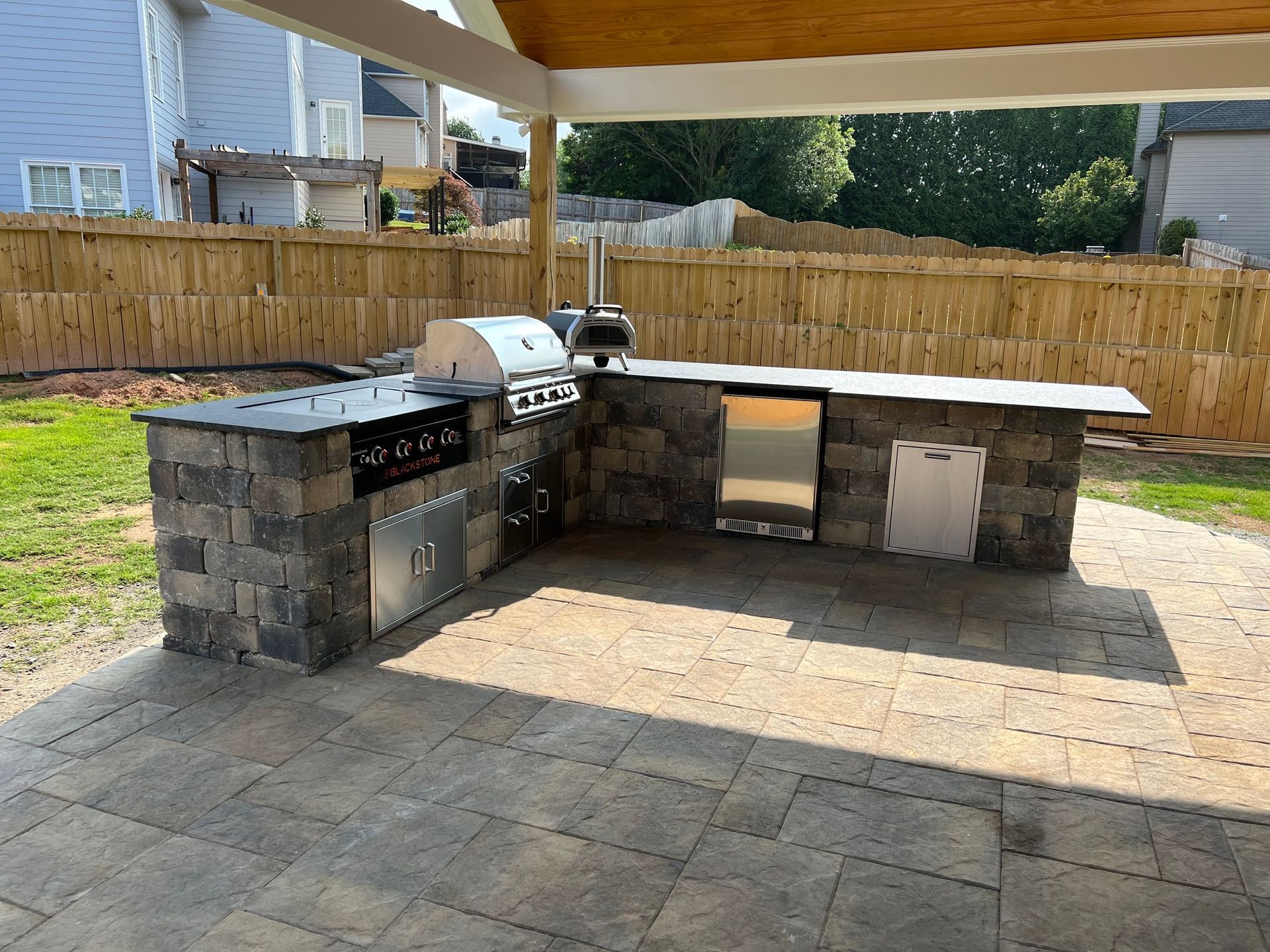 Outdoor kitchen with grill, pizza oven, and built-in storage on a paved patio.