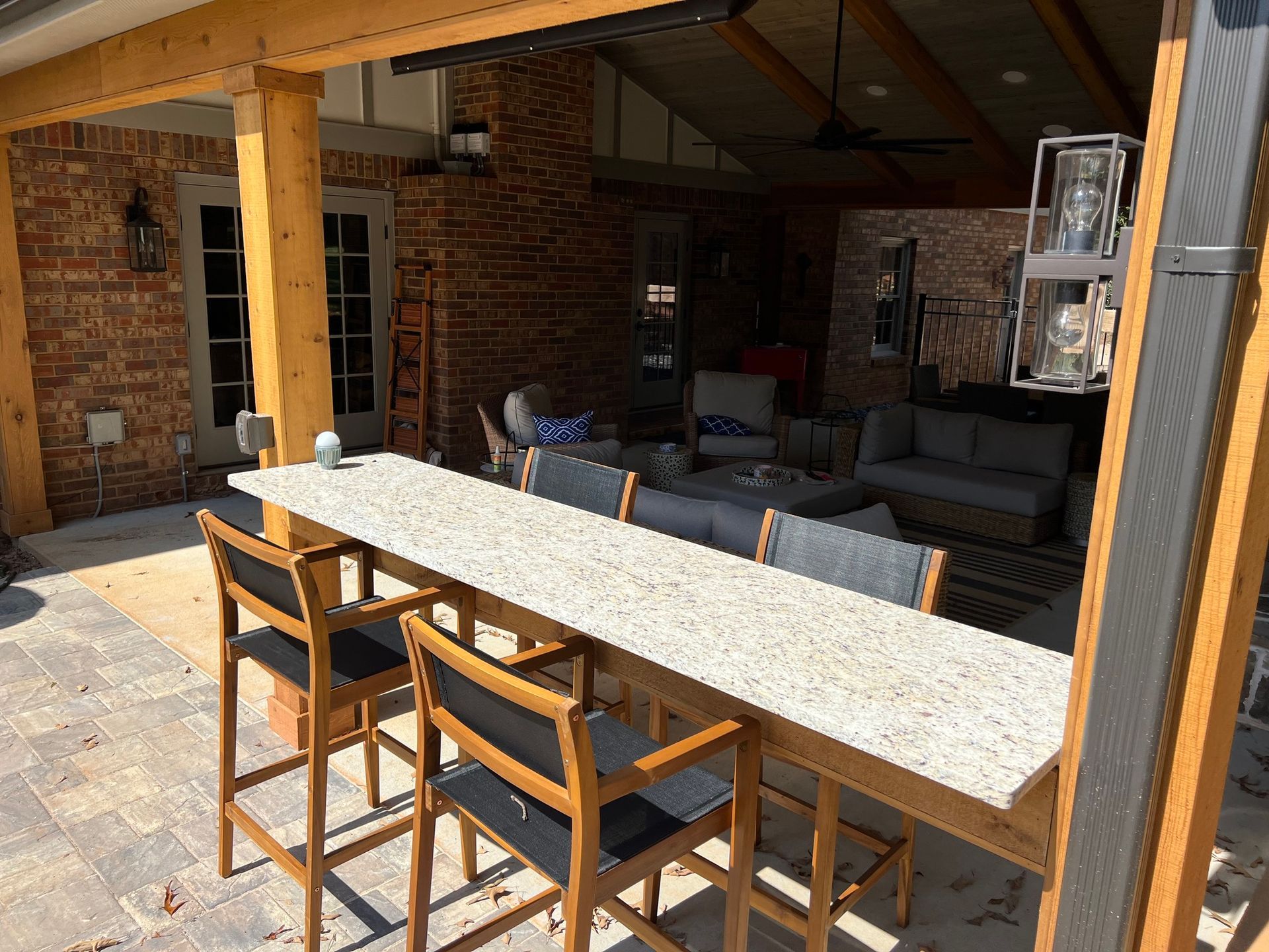 Outdoor patio with bar seating, gray countertop, wooden chairs, brick wall, and outdoor furniture.