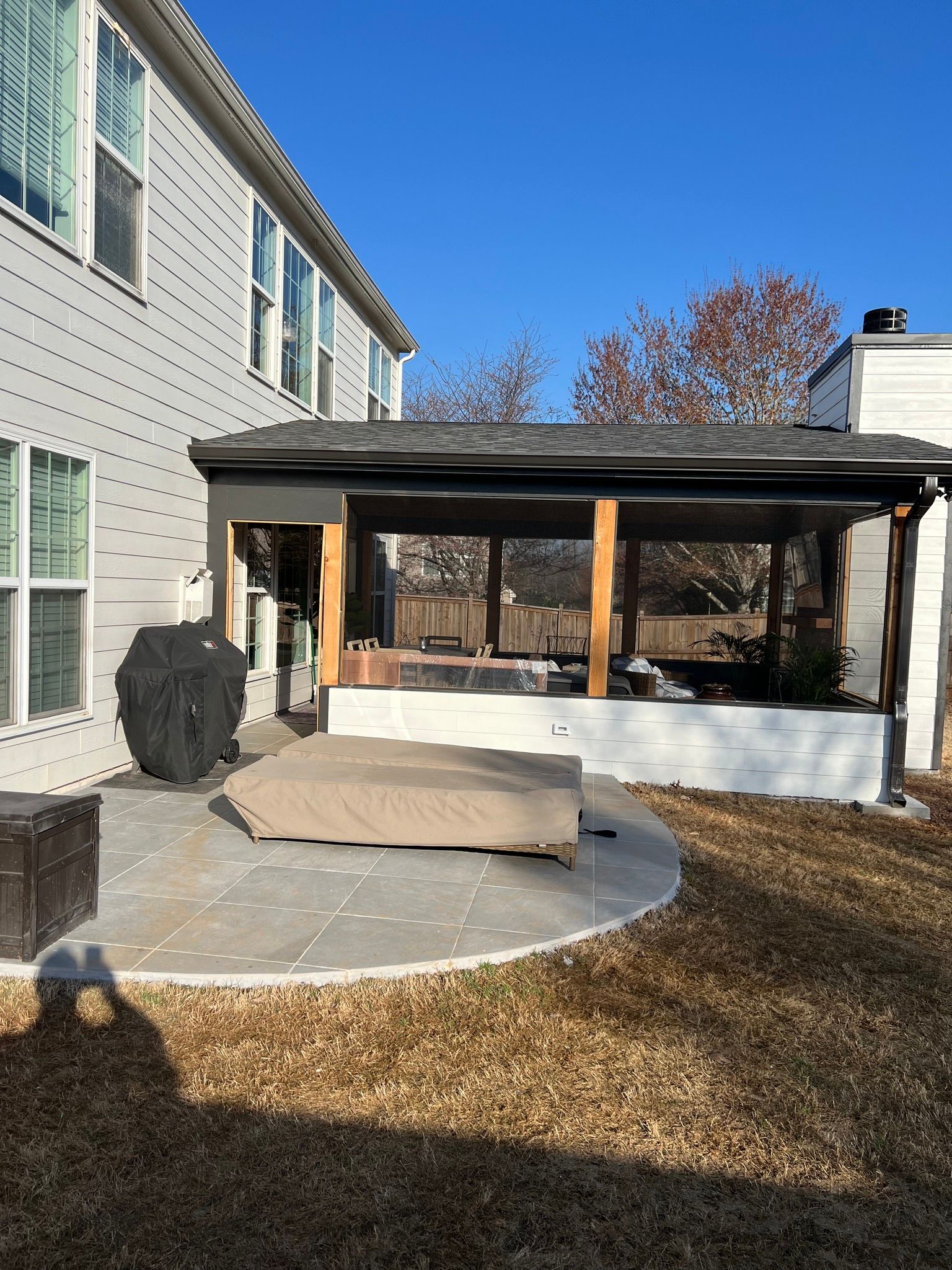 Patio with covered seating, tan grass, and house under a blue sky.