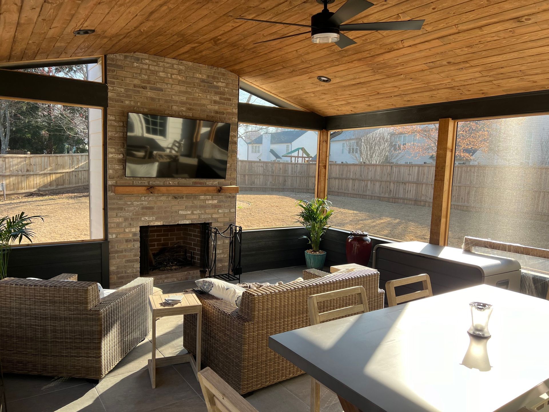 Screened-in patio with fireplace, wicker furniture, and a table overlooking a fenced yard.