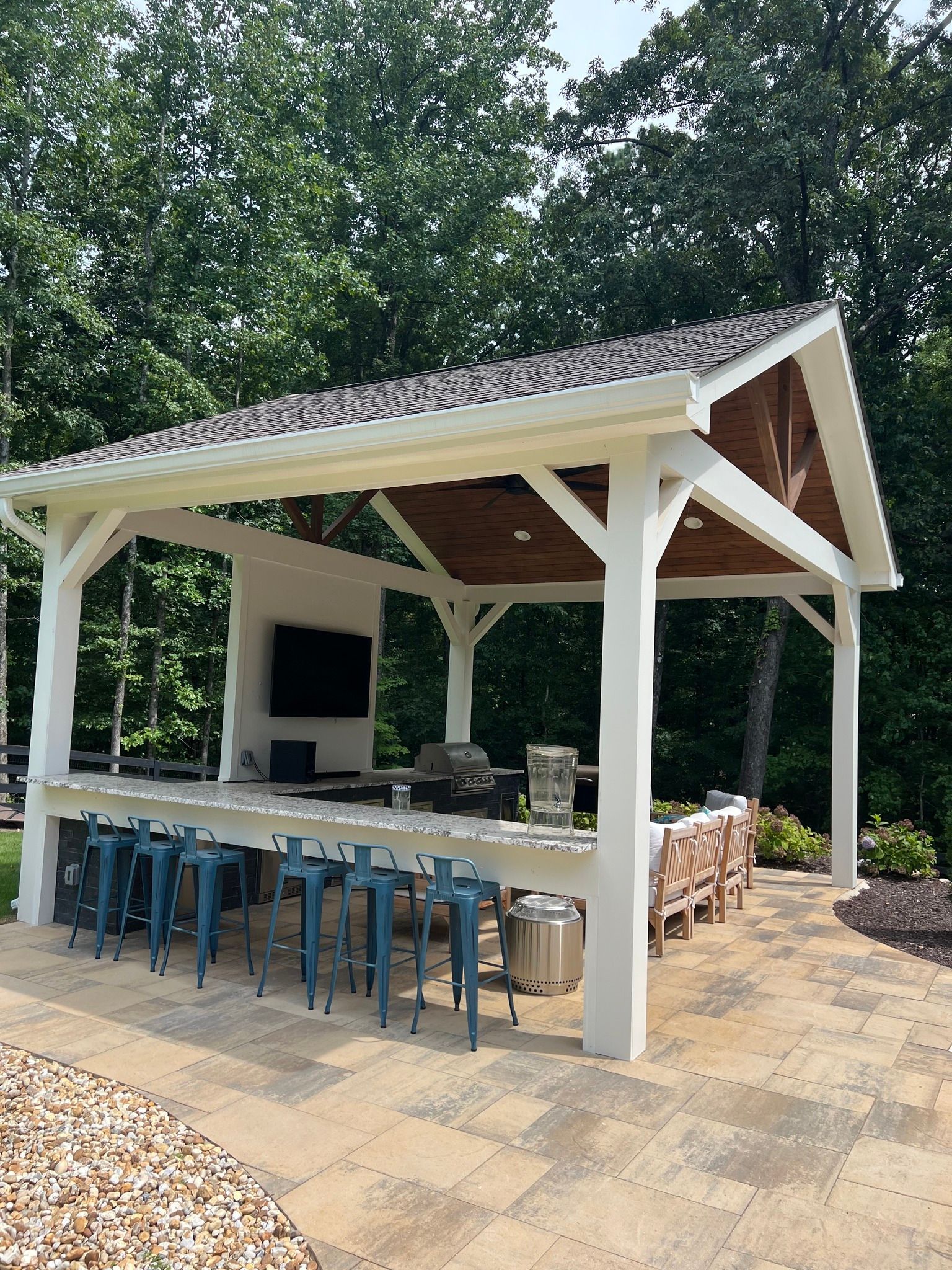 Outdoor kitchen with white pergola, bar seating, grill, and TV.