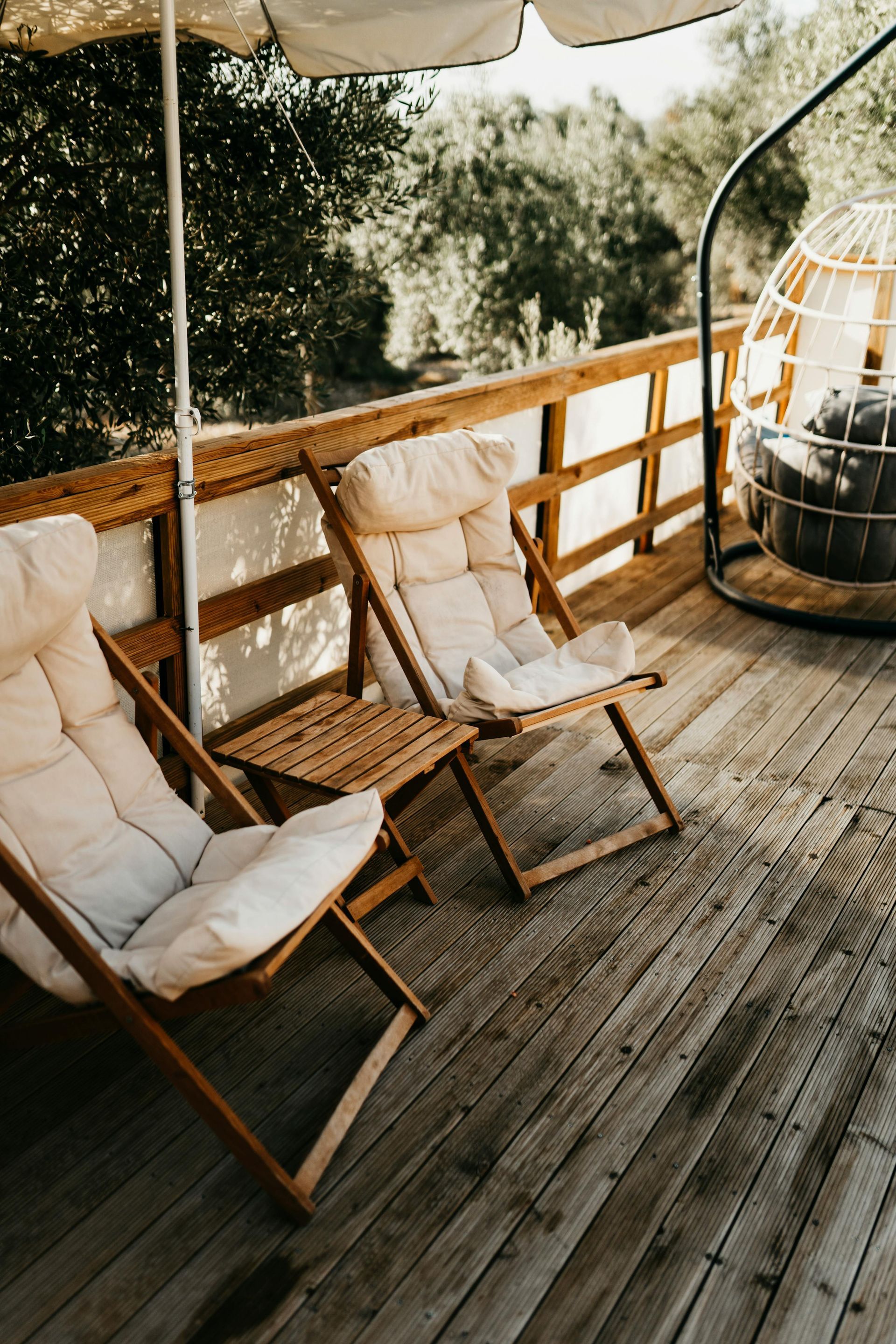 Wooden deck with two folding chairs, side table, and hanging chair, shaded by an umbrella.
