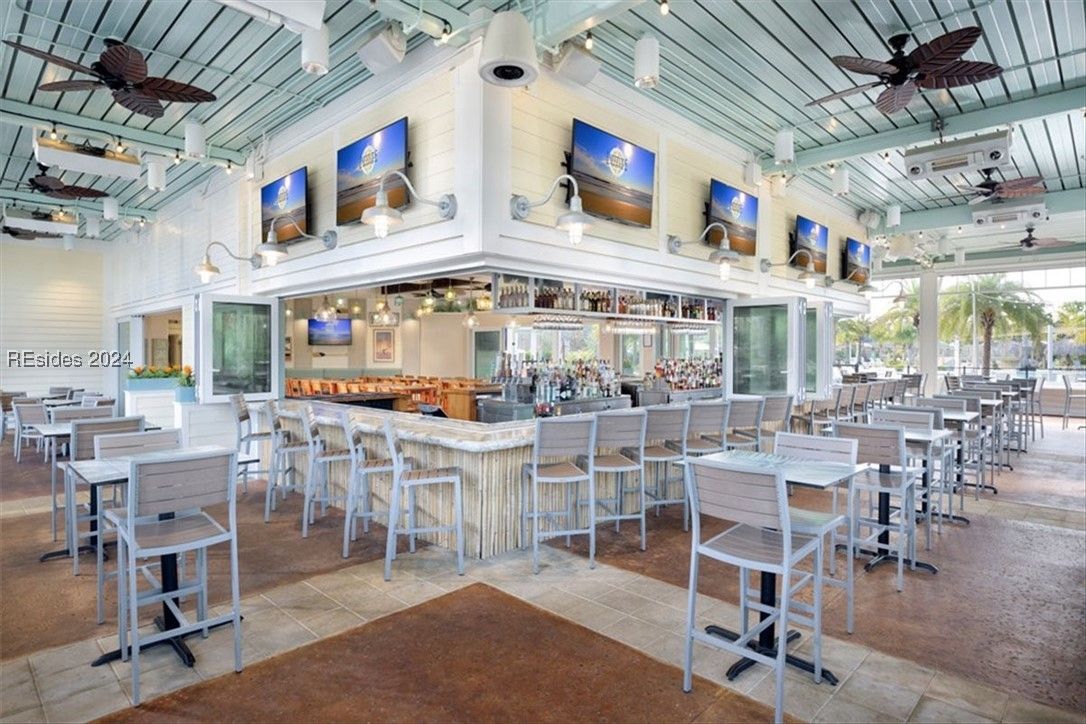 Outdoor bar area with TVs, high tables, bar stools, and palm trees in the background.