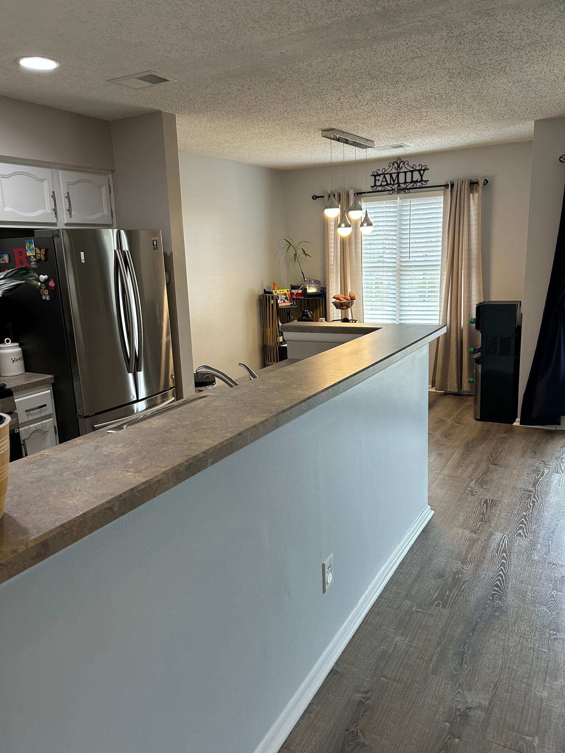 Kitchen with countertop, stainless steel appliances, and dining area with window and curtains.