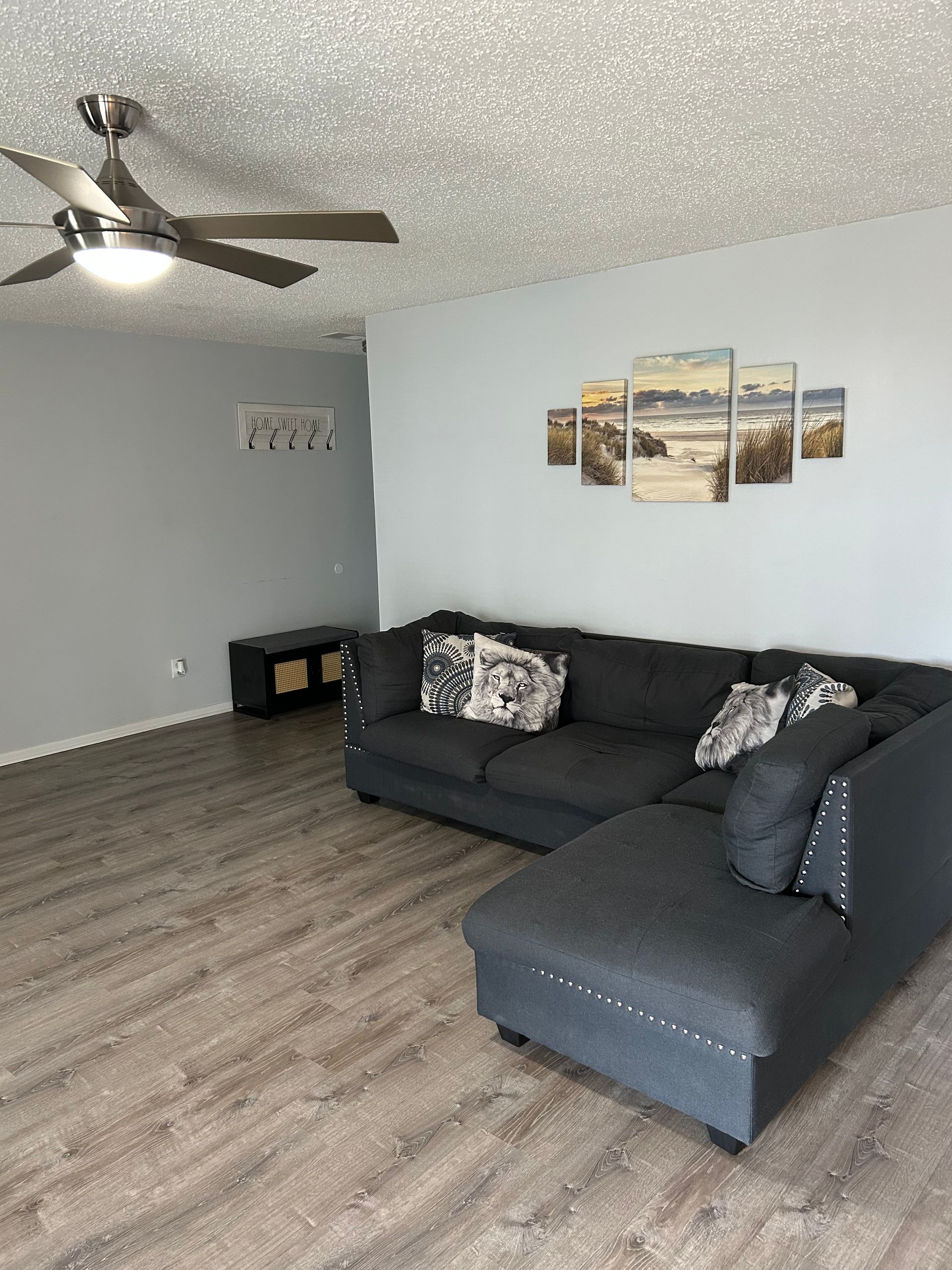 Living room with gray walls, sectional sofa, art, and ceiling fan.