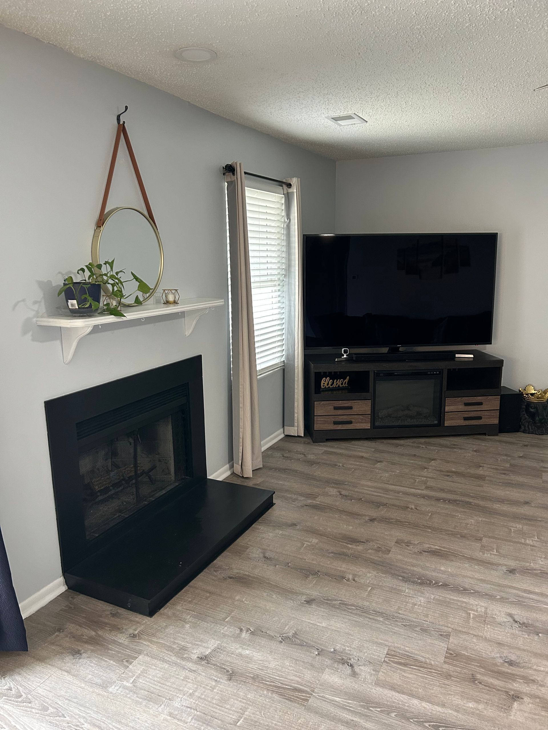 Living room with gray walls, fireplace, TV on stand, mirror, and a window with curtain.