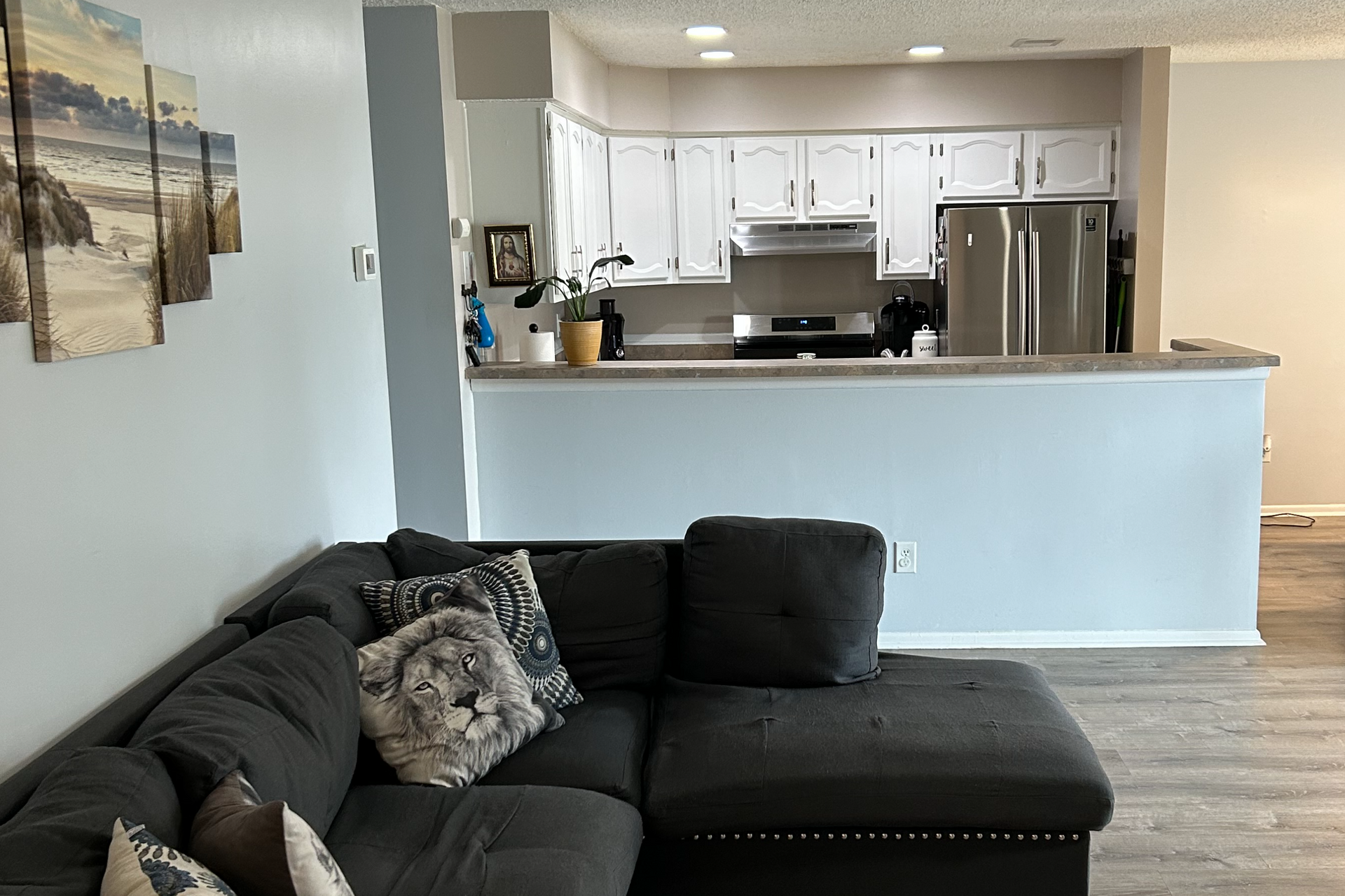 Living room with a gray sectional sofa and a view of the kitchen with white cabinets.