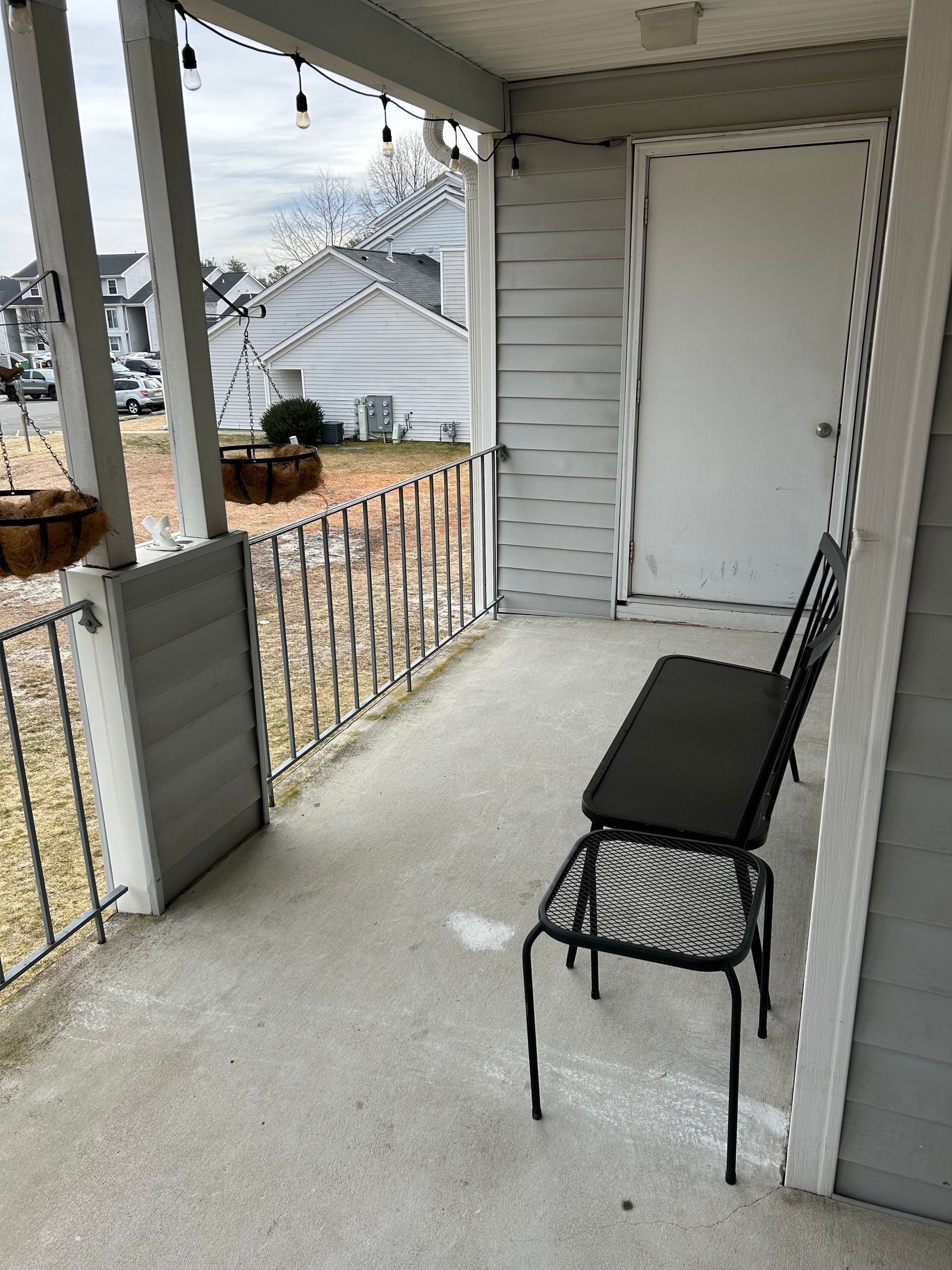 Small covered patio with a black bench and chair. A door is on the right, and a decorative fence runs along the patio's edge.