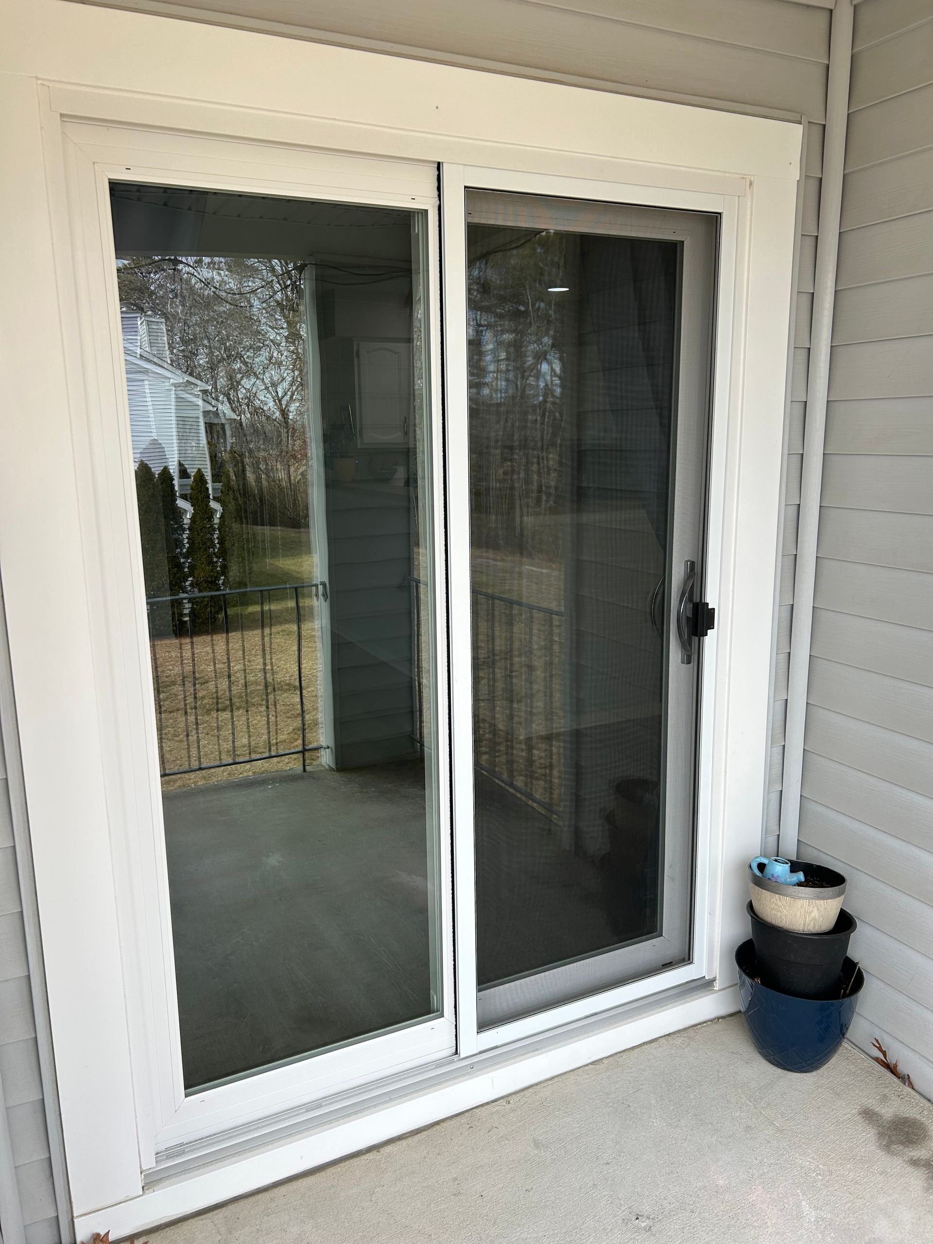 White sliding glass door with screen, leading to a patio. Three stacked flower pots sit to the right.
