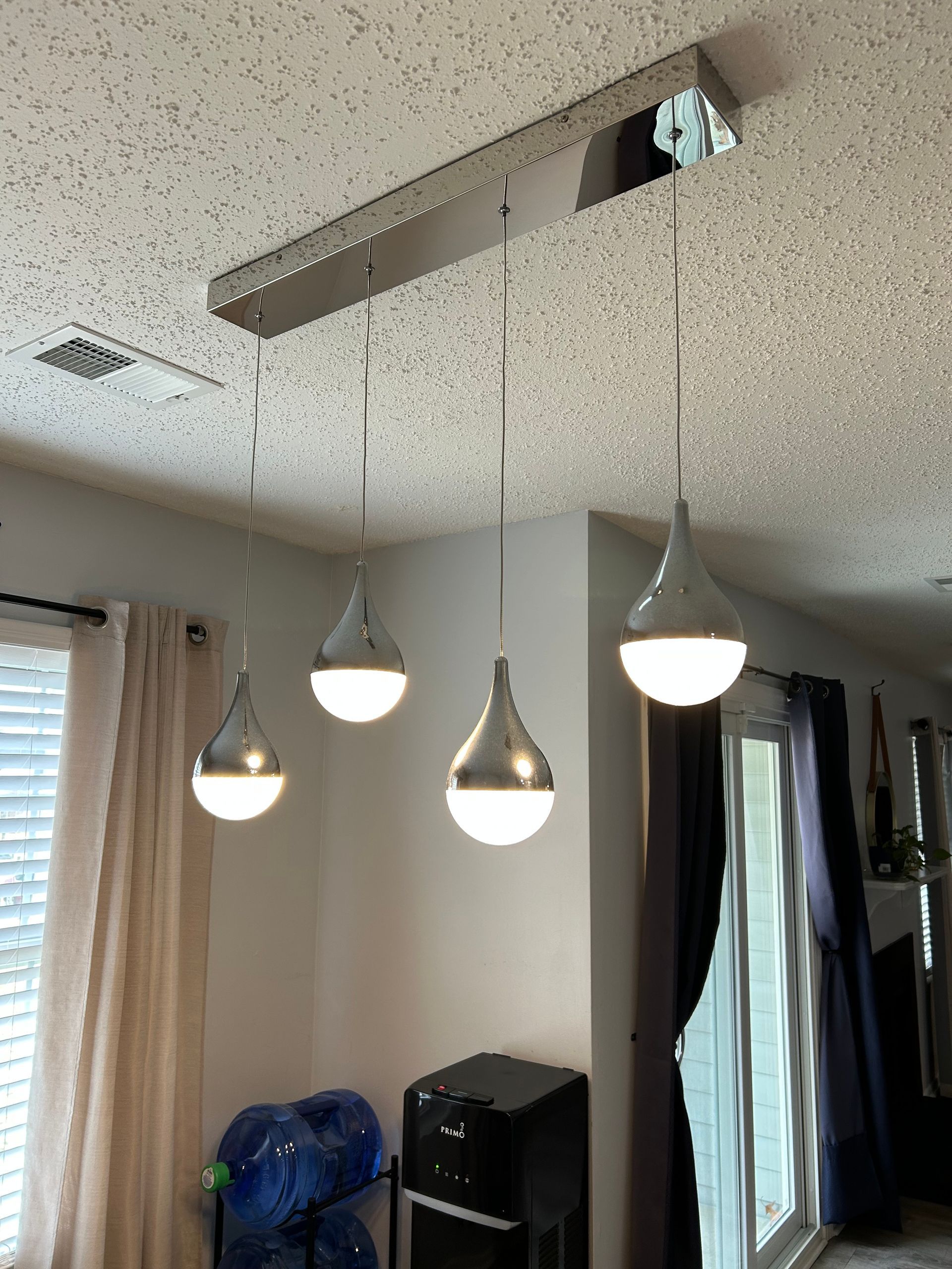 Four silver teardrop pendant lights suspended from a rectangular fixture on a textured ceiling.