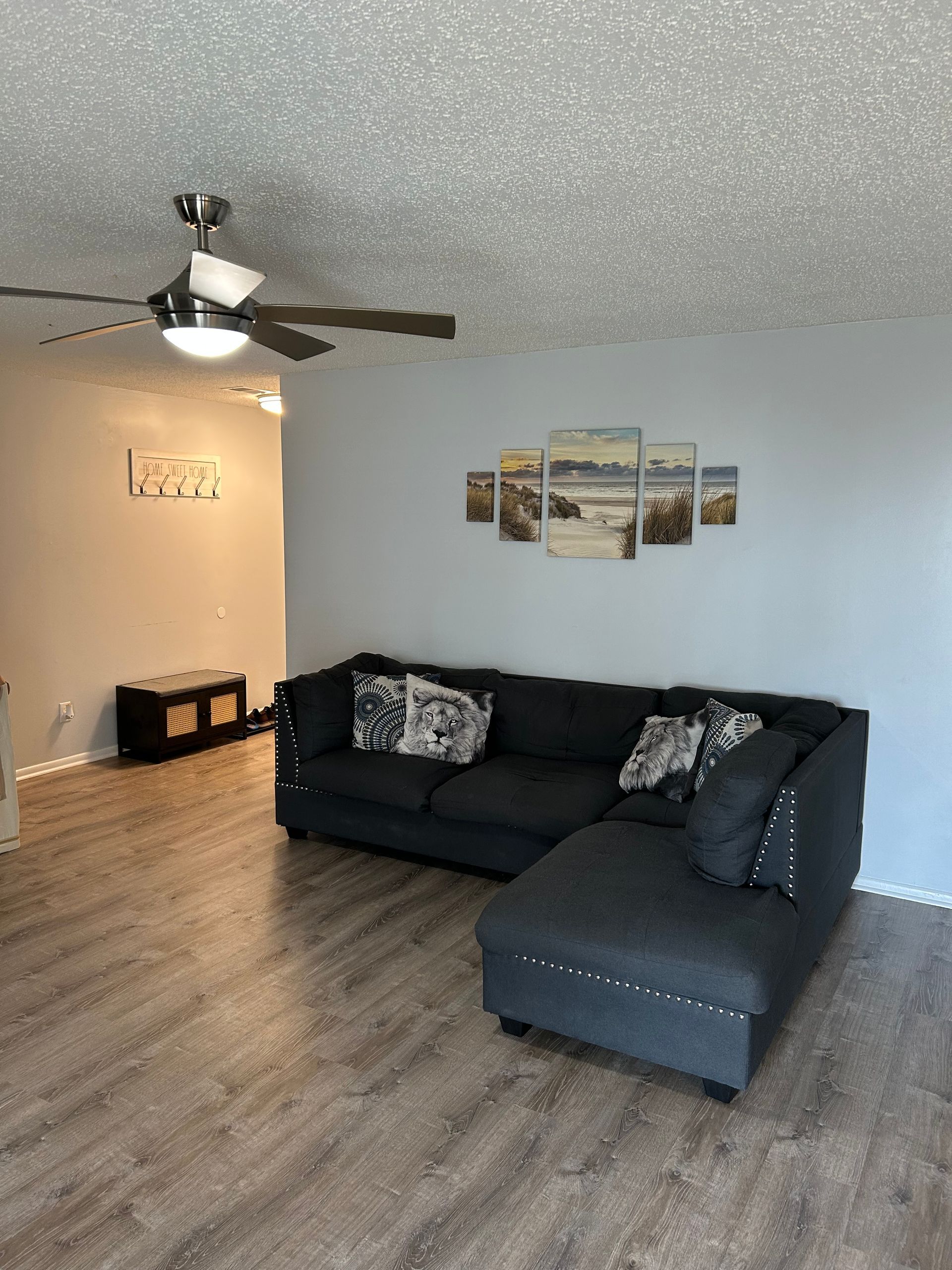 Living room with gray sectional sofa, art on wall, and ceiling fan. Wooden floor.