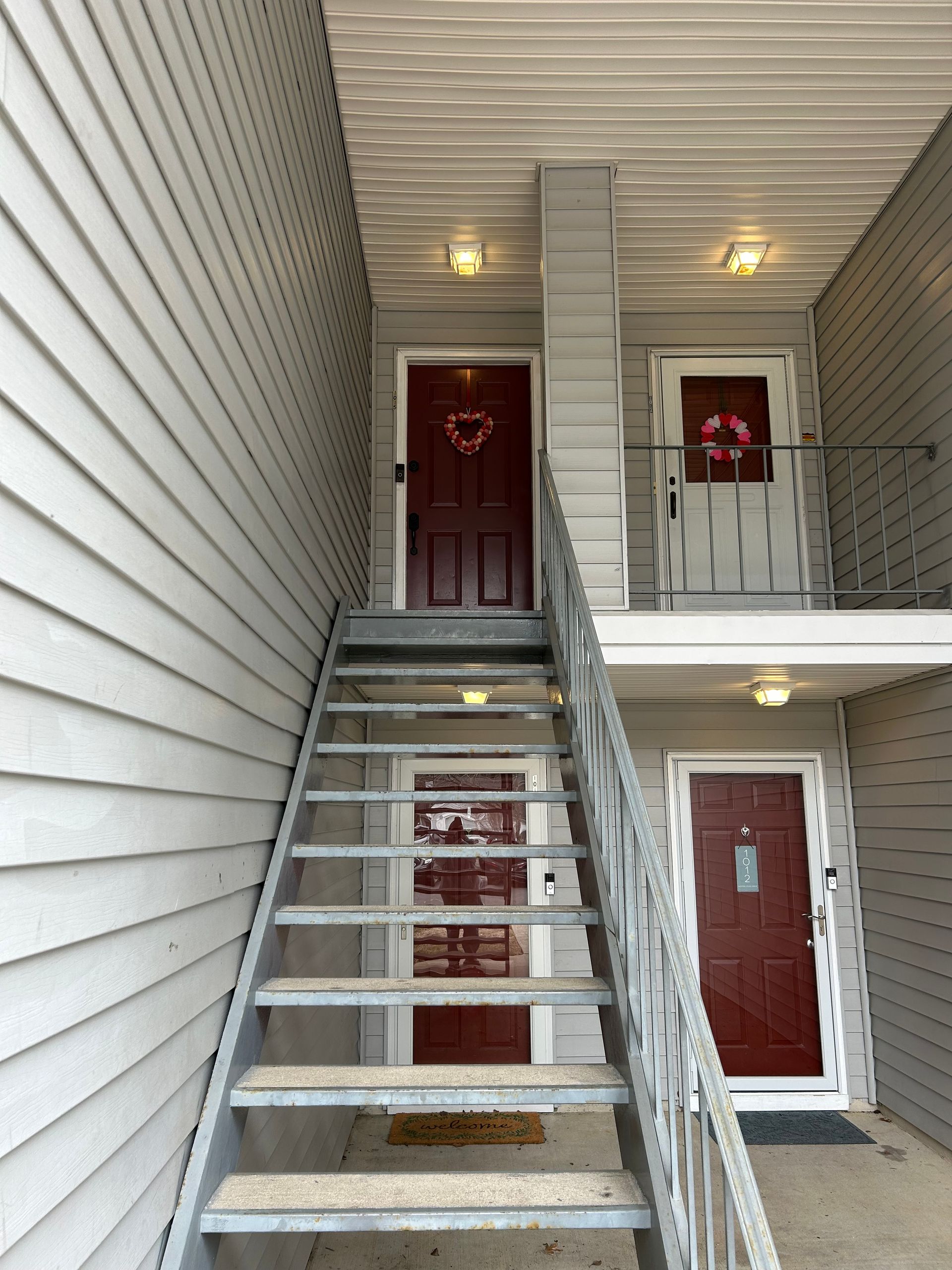 Exterior view of apartment building with metal stairs leading to doors. Red and white doors.