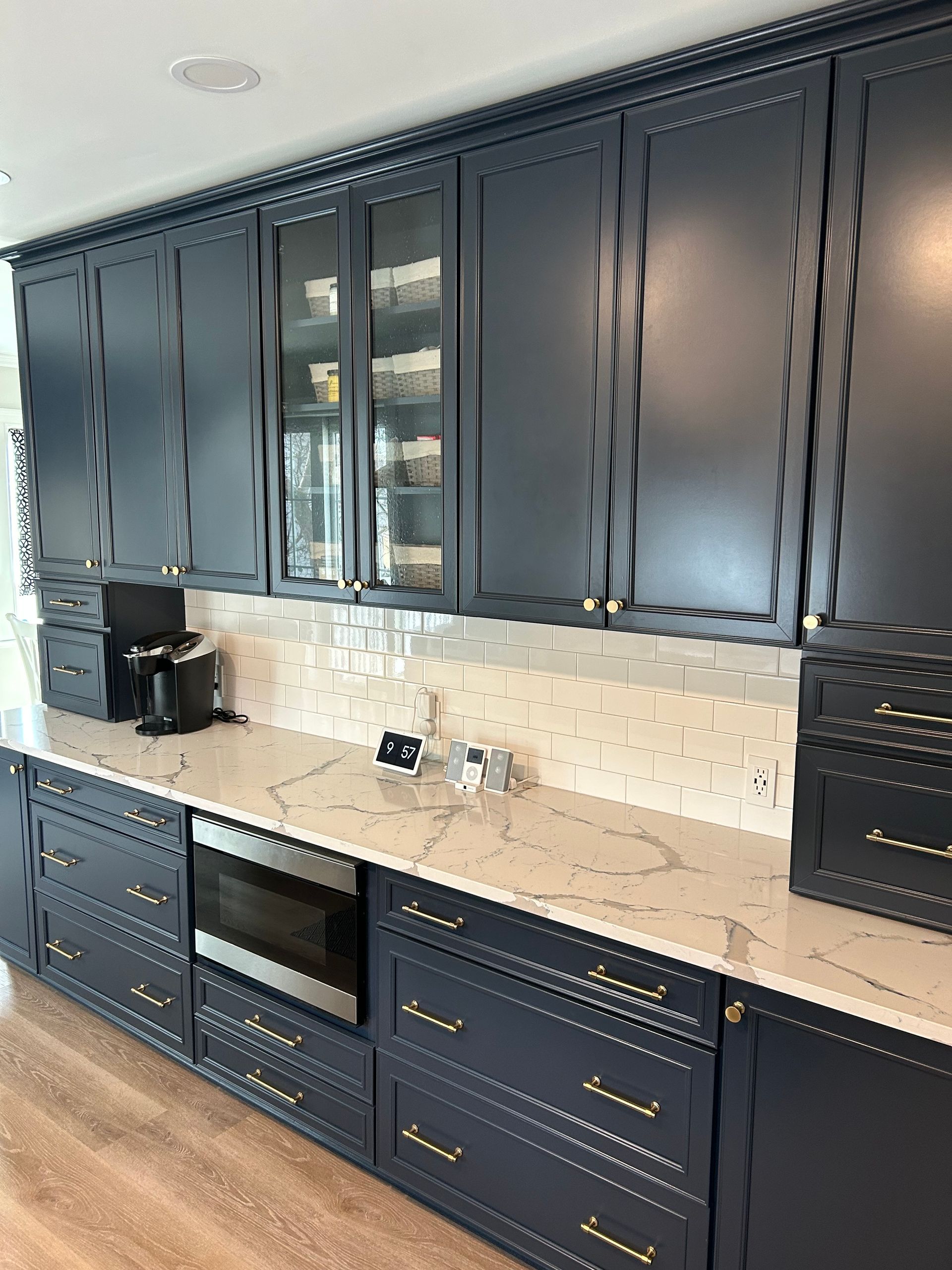 Dark blue kitchen cabinets with gold hardware, white countertop, and glass-door upper cabinets.