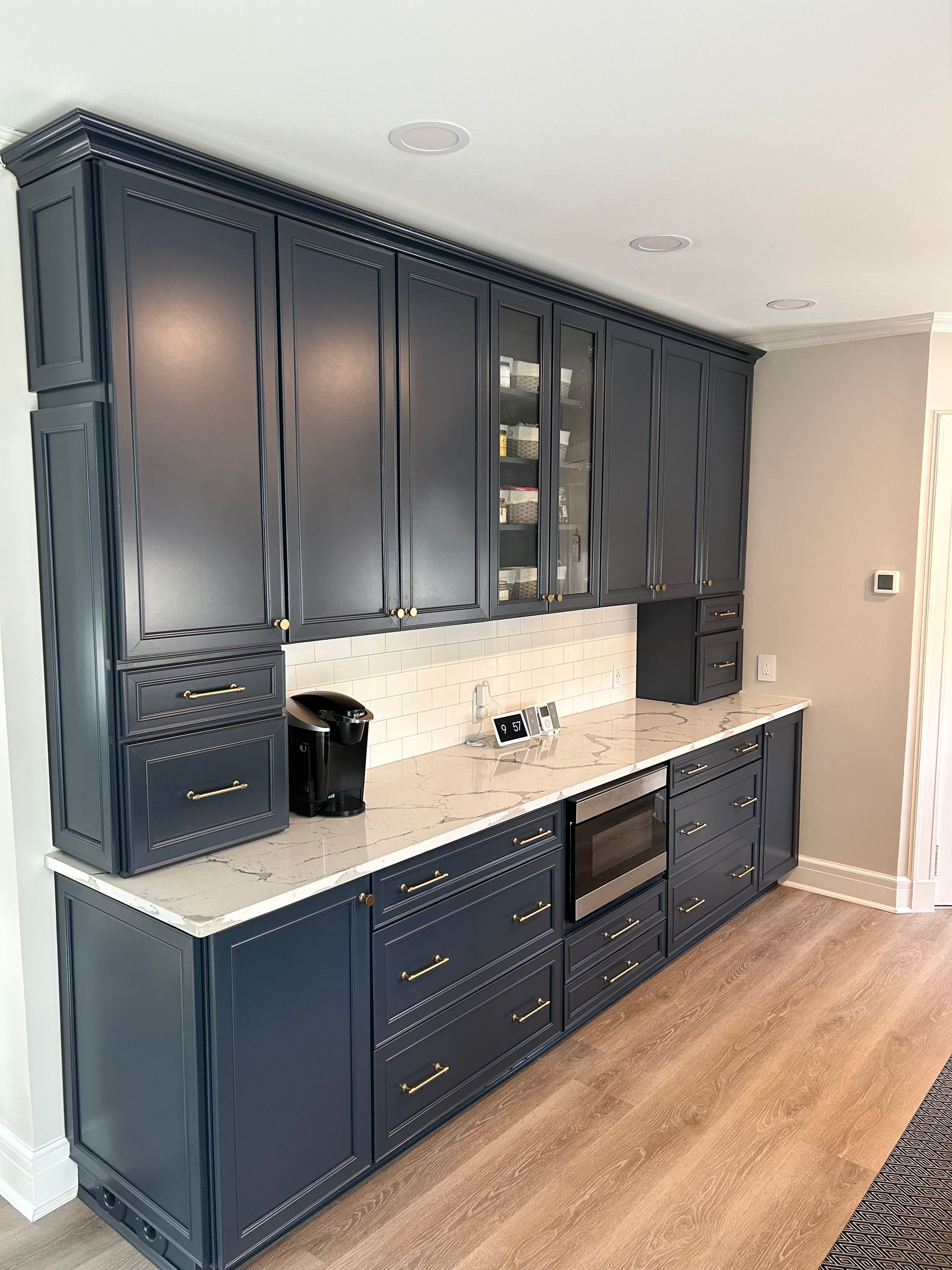 Navy blue kitchen cabinets with a light countertop. Built-in microwave, coffee maker, and glass-door upper cabinets.