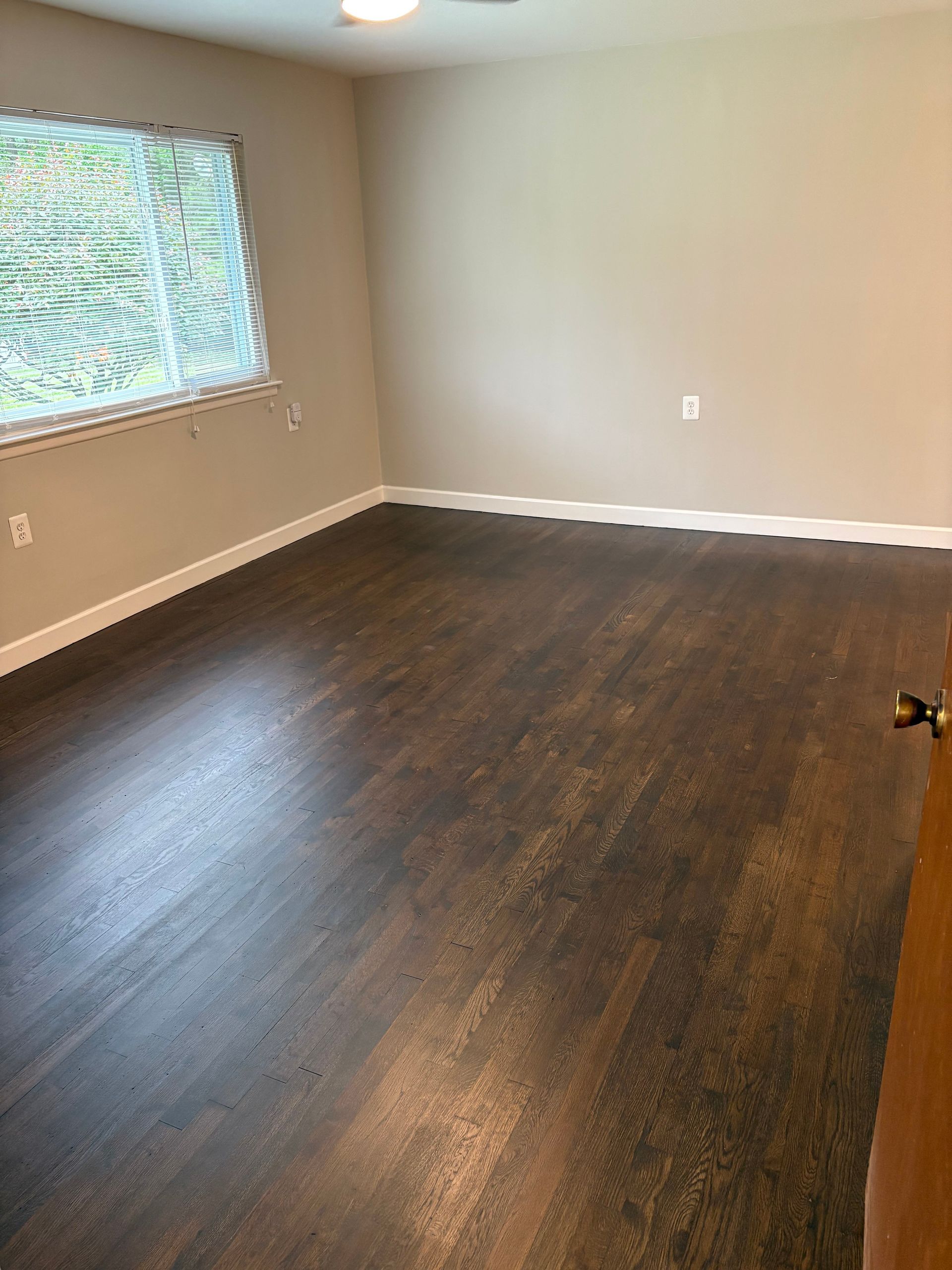 Empty room with dark wood-look flooring, beige walls, a window, and white trim.