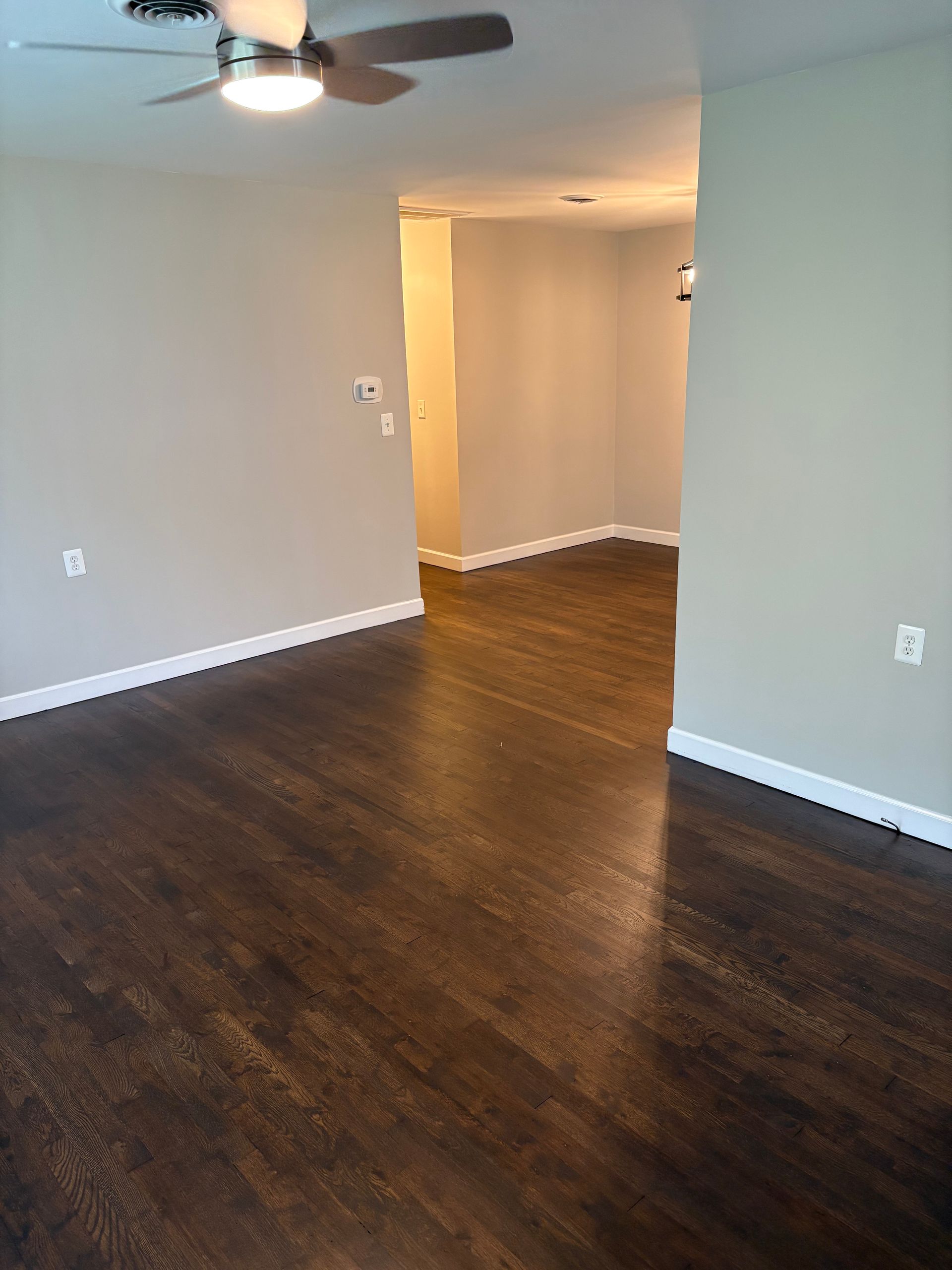Empty living room with dark wood floor, light gray walls, and an entryway.