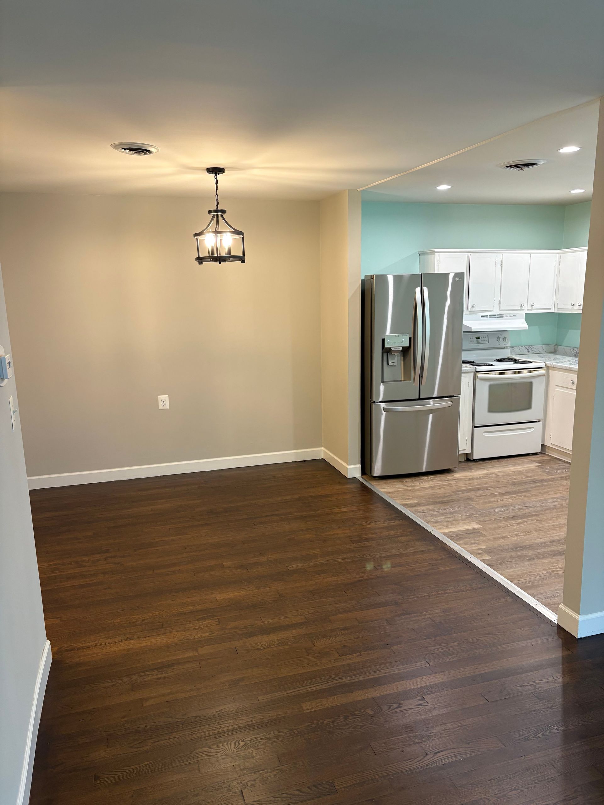 Dining room with dark wood floor, light walls, and a view into a kitchen with stainless steel appliances.