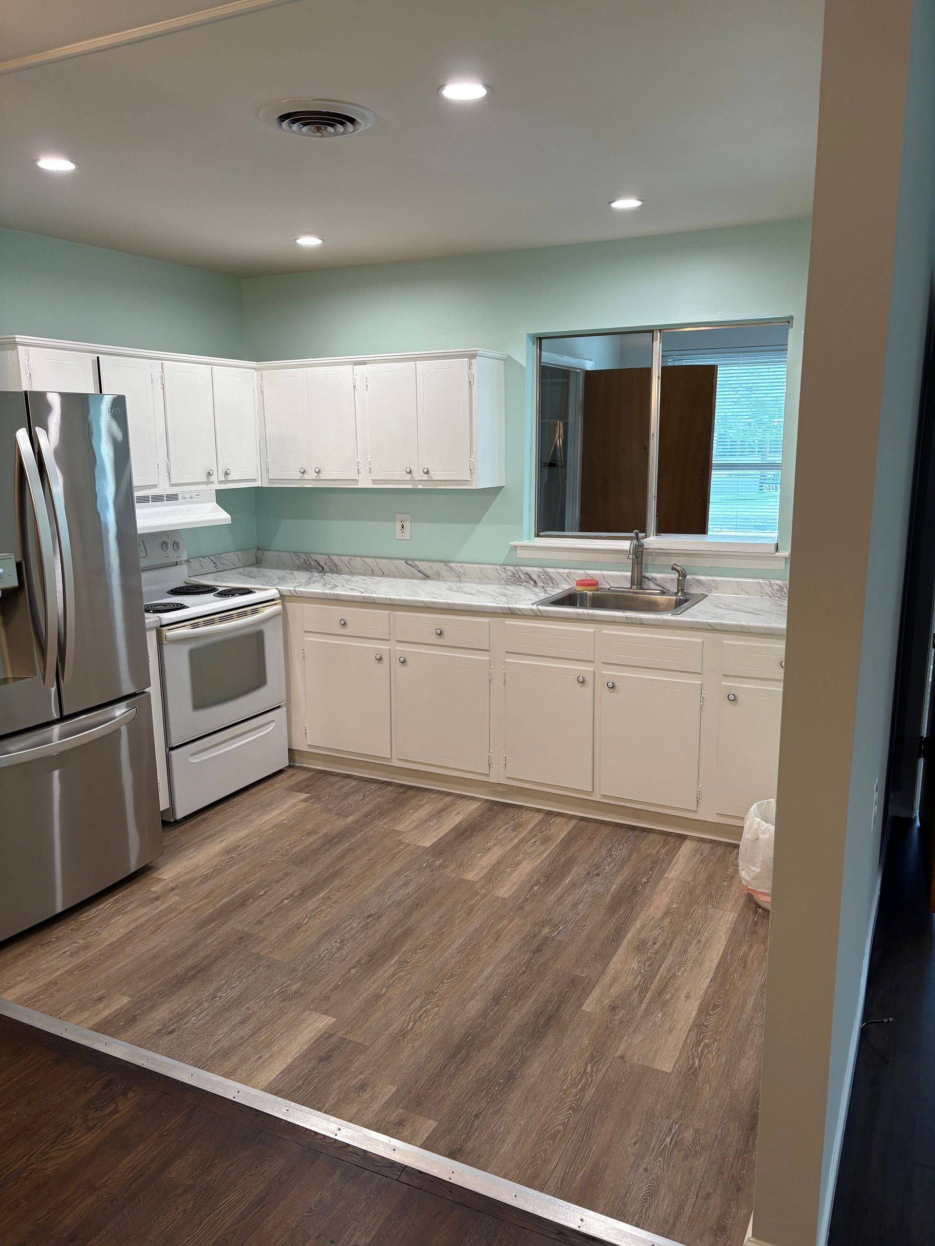 A kitchen with white cabinets, stainless steel appliances, light countertops, and wood-look flooring.