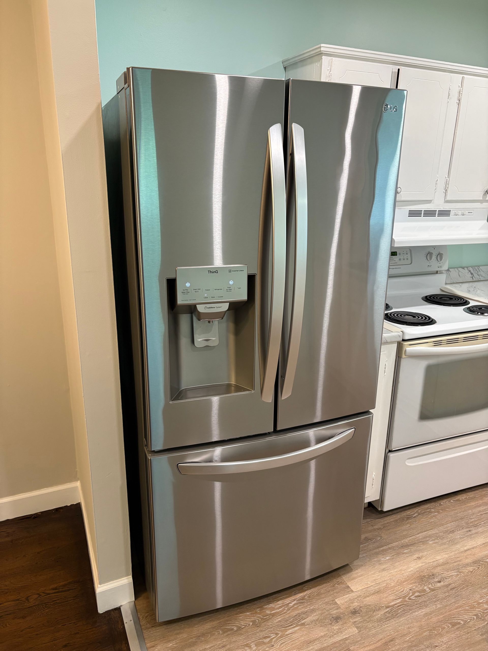 Stainless steel refrigerator in a kitchen. Has water/ice dispenser on the left door. Bottom freezer drawer.