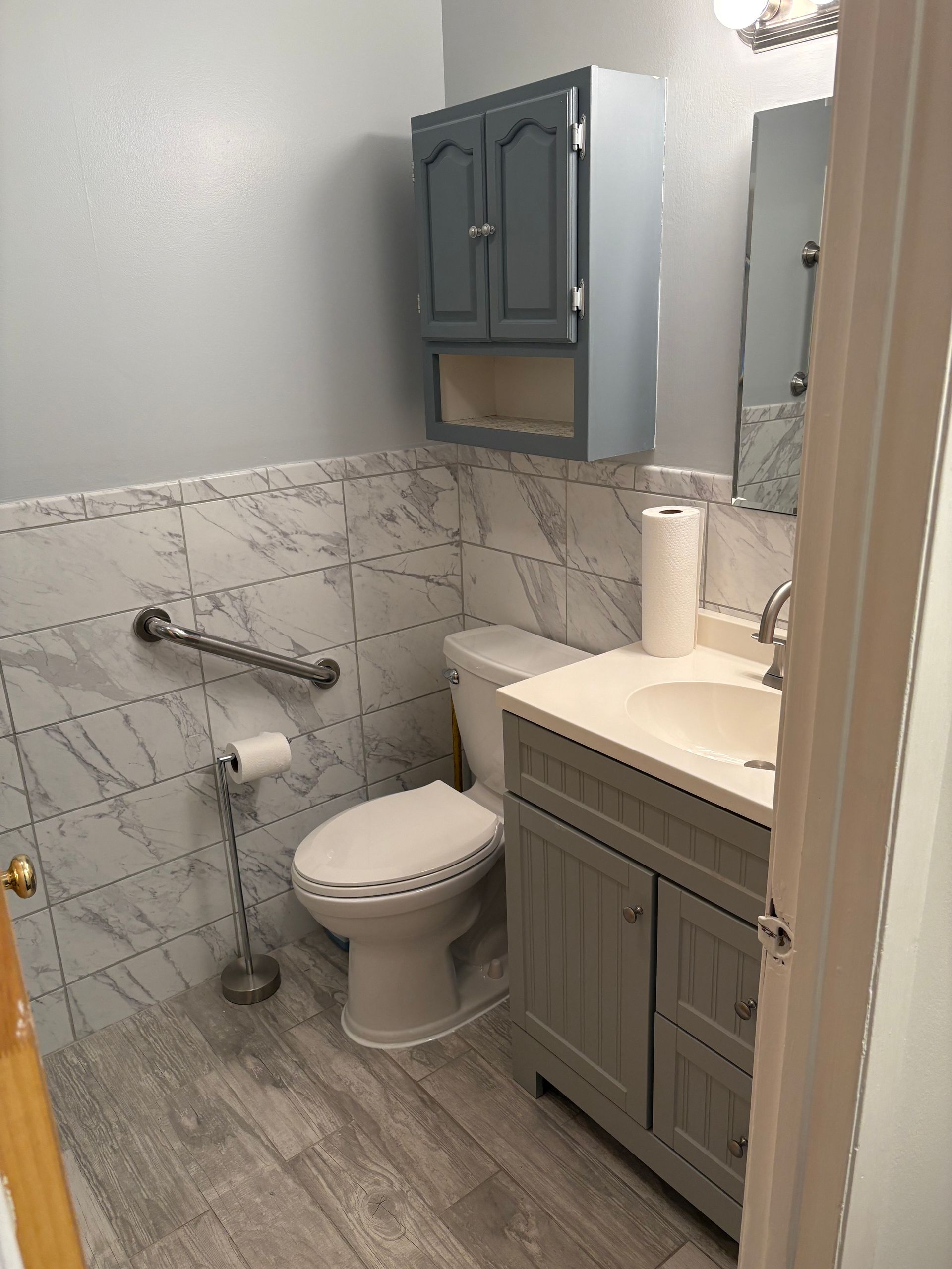 Bathroom with gray walls, marble tile, gray vanity, toilet, and grab bar.