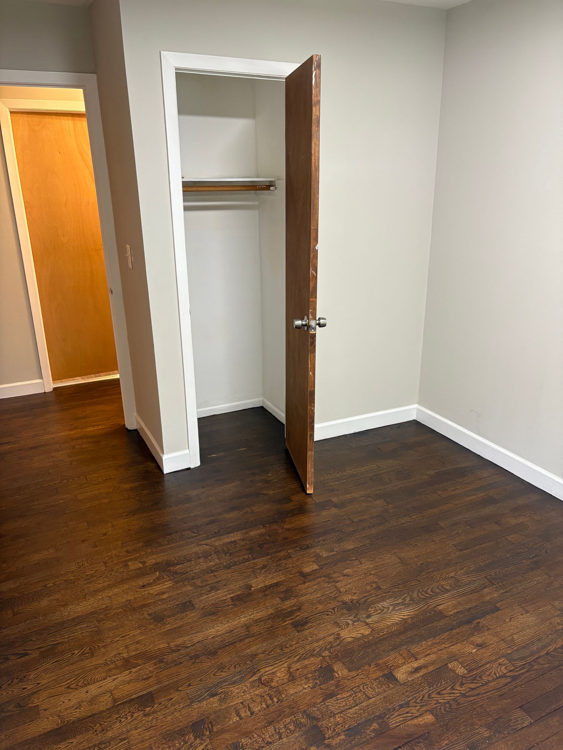 Empty room with dark wood-look flooring, closet with open door, and doorway to another room.
