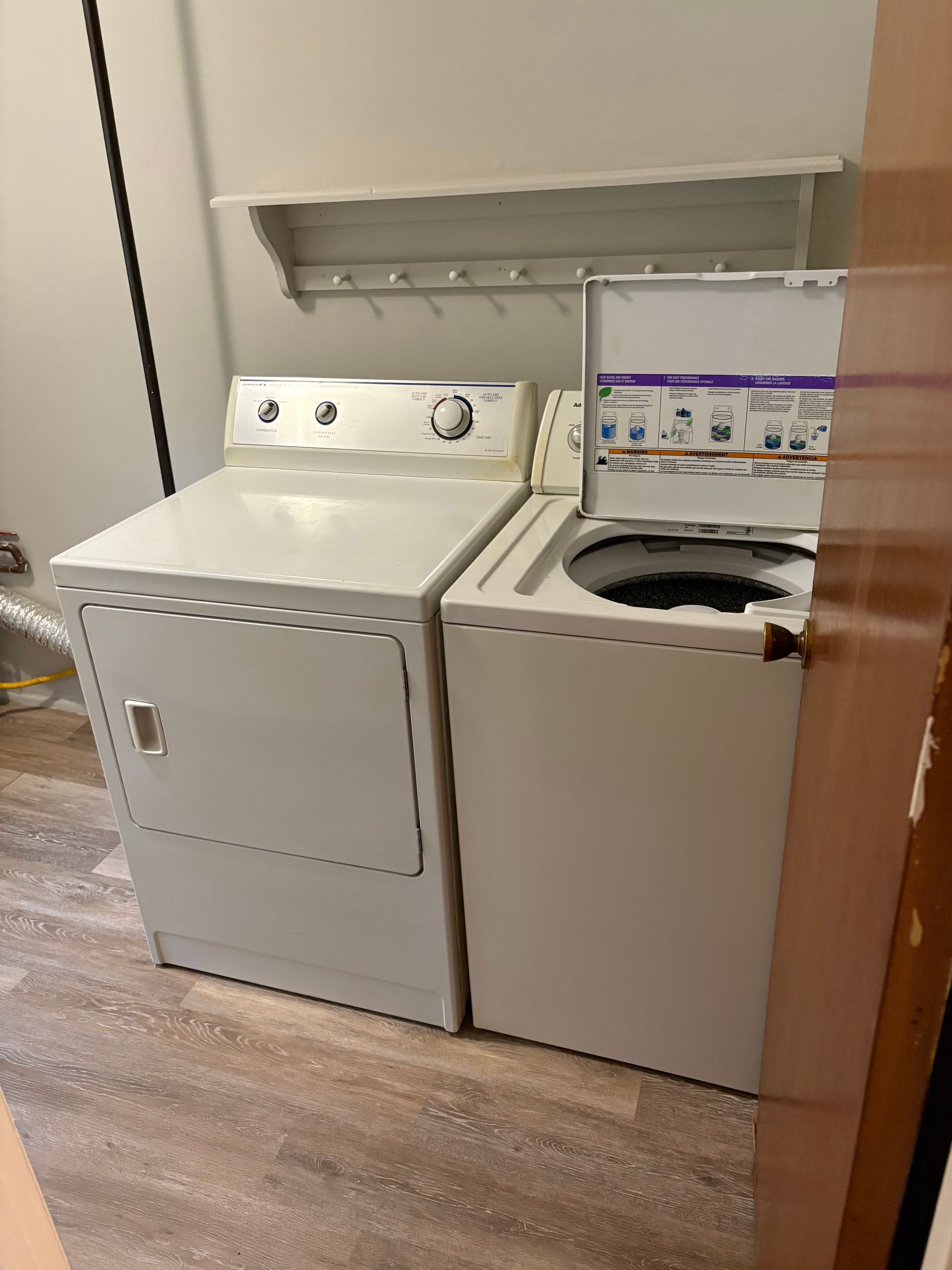 White washer and dryer set in a laundry room, with a shelf and clothing rack above.