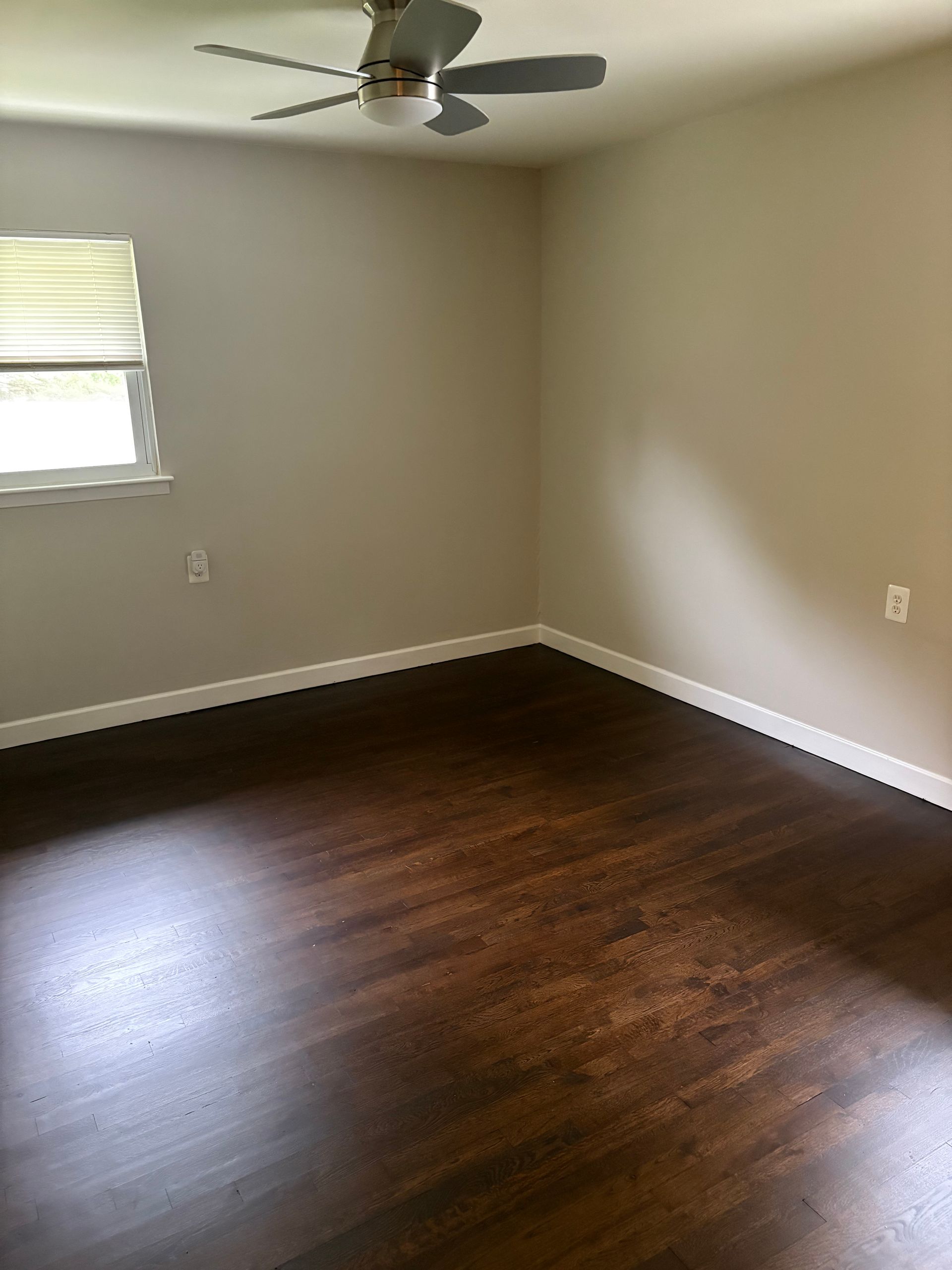 Empty room with dark wood flooring, light walls, and a ceiling fan.