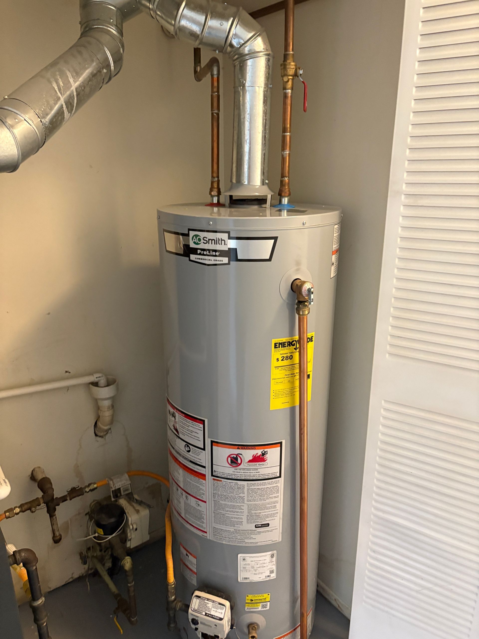 A gray water heater with copper pipes, a vent, and energy efficiency sticker is in a utility room.