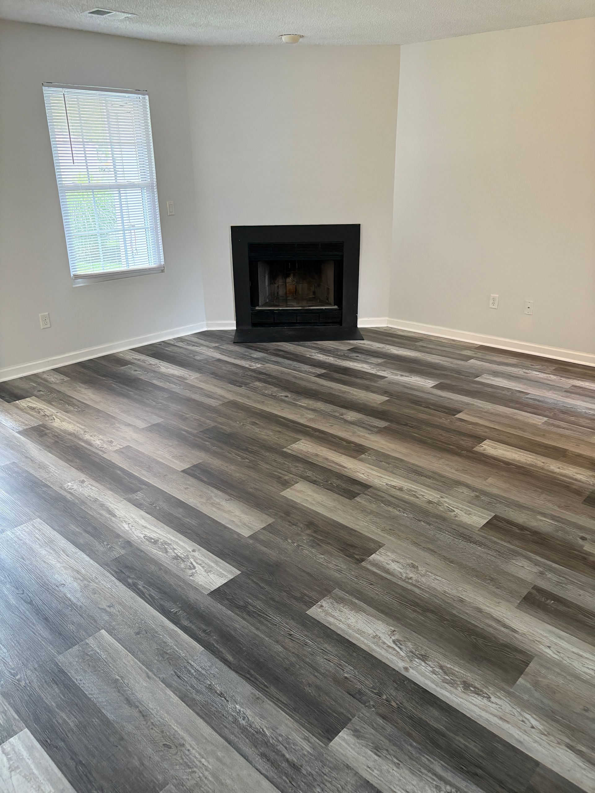 Empty room with gray wood-look flooring, fireplace, and window with blinds.