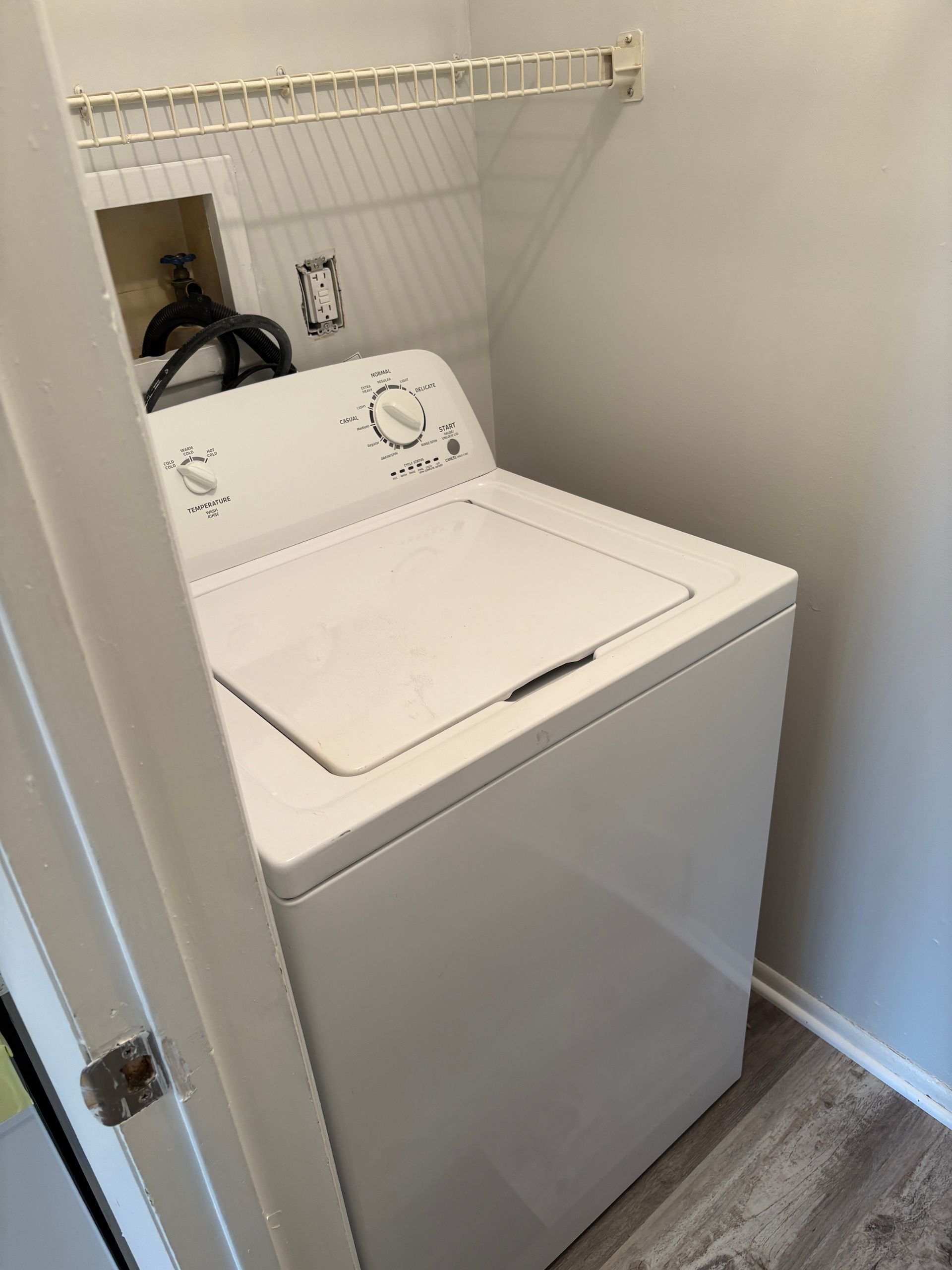 White top-load washing machine in a small laundry area with shelving above.