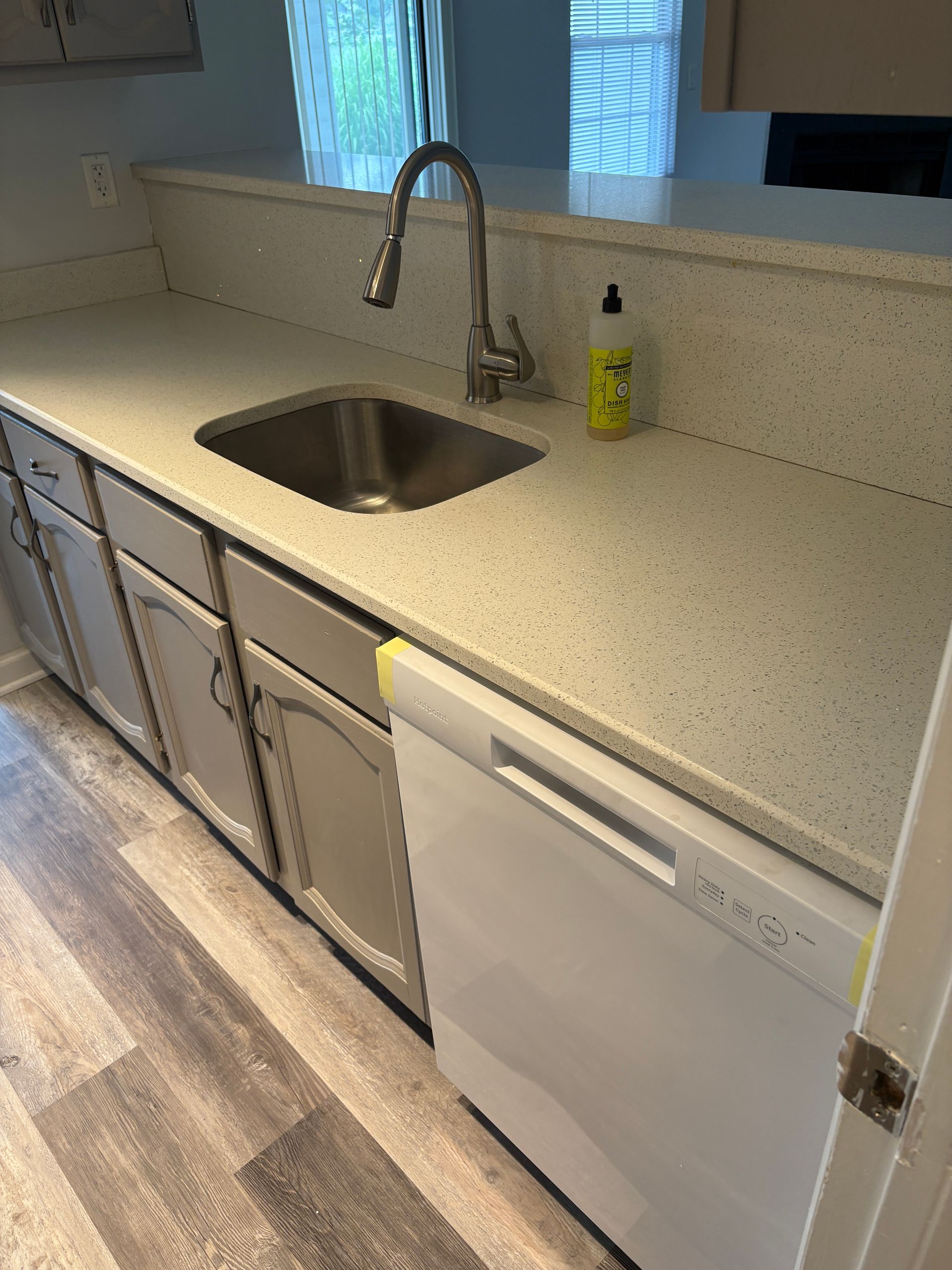 Kitchen with white cabinets, stainless steel sink, speckled countertop, and dishwasher.
