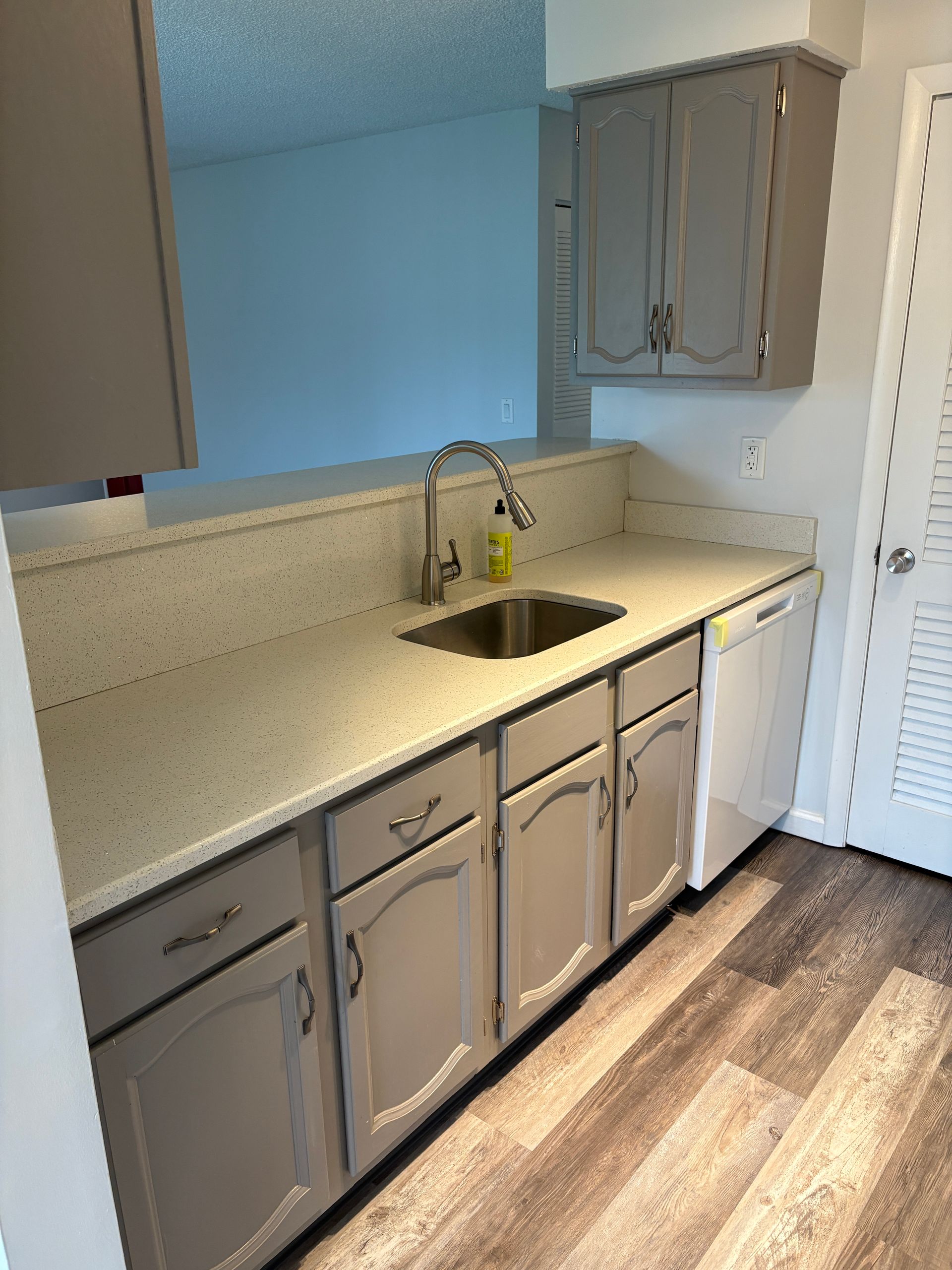 Kitchen with gray cabinets, white countertop, stainless steel sink, and dishwasher.