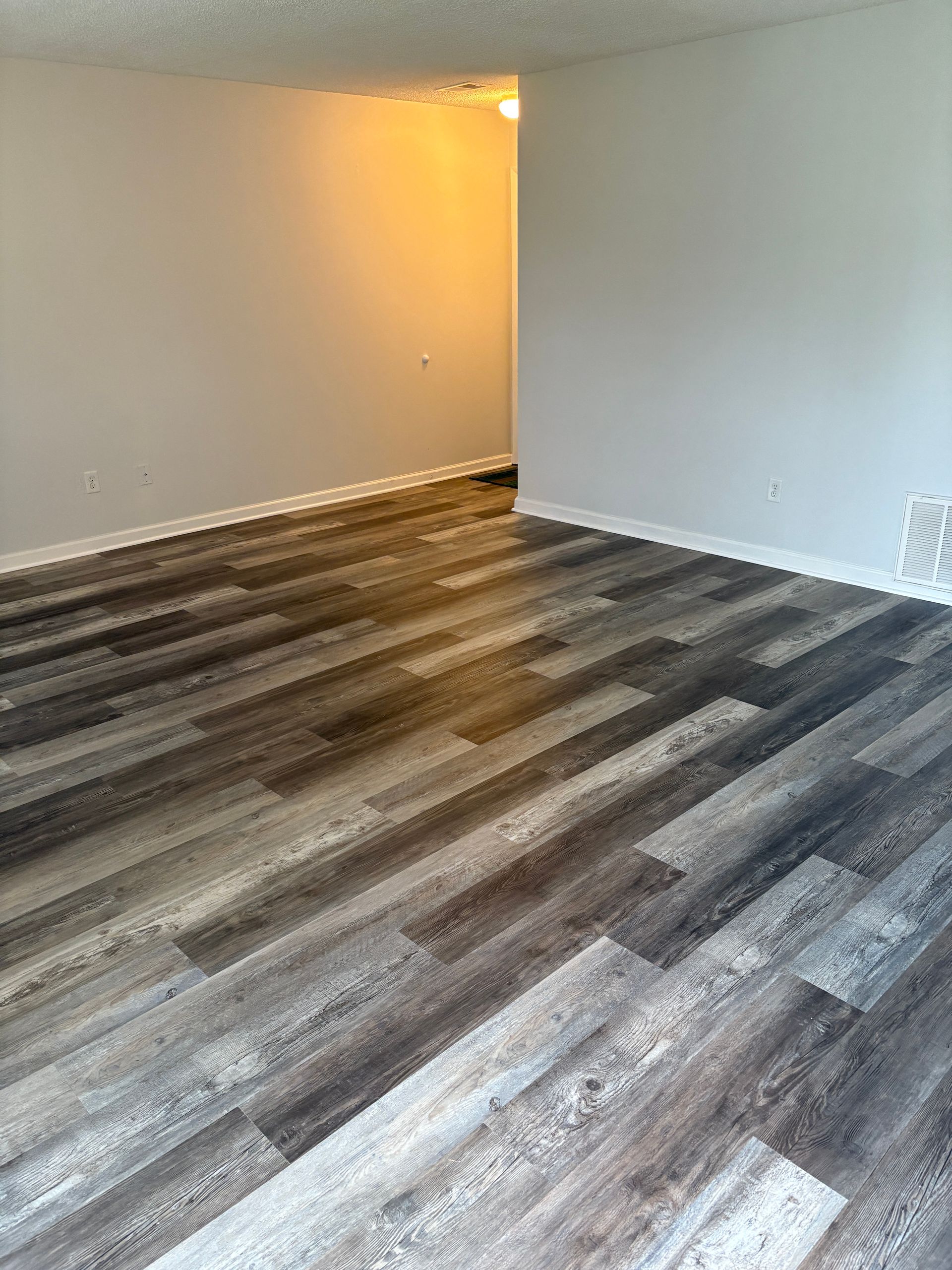 Room with gray wood-look flooring, light gray walls. An open doorway leads to a lighter room.