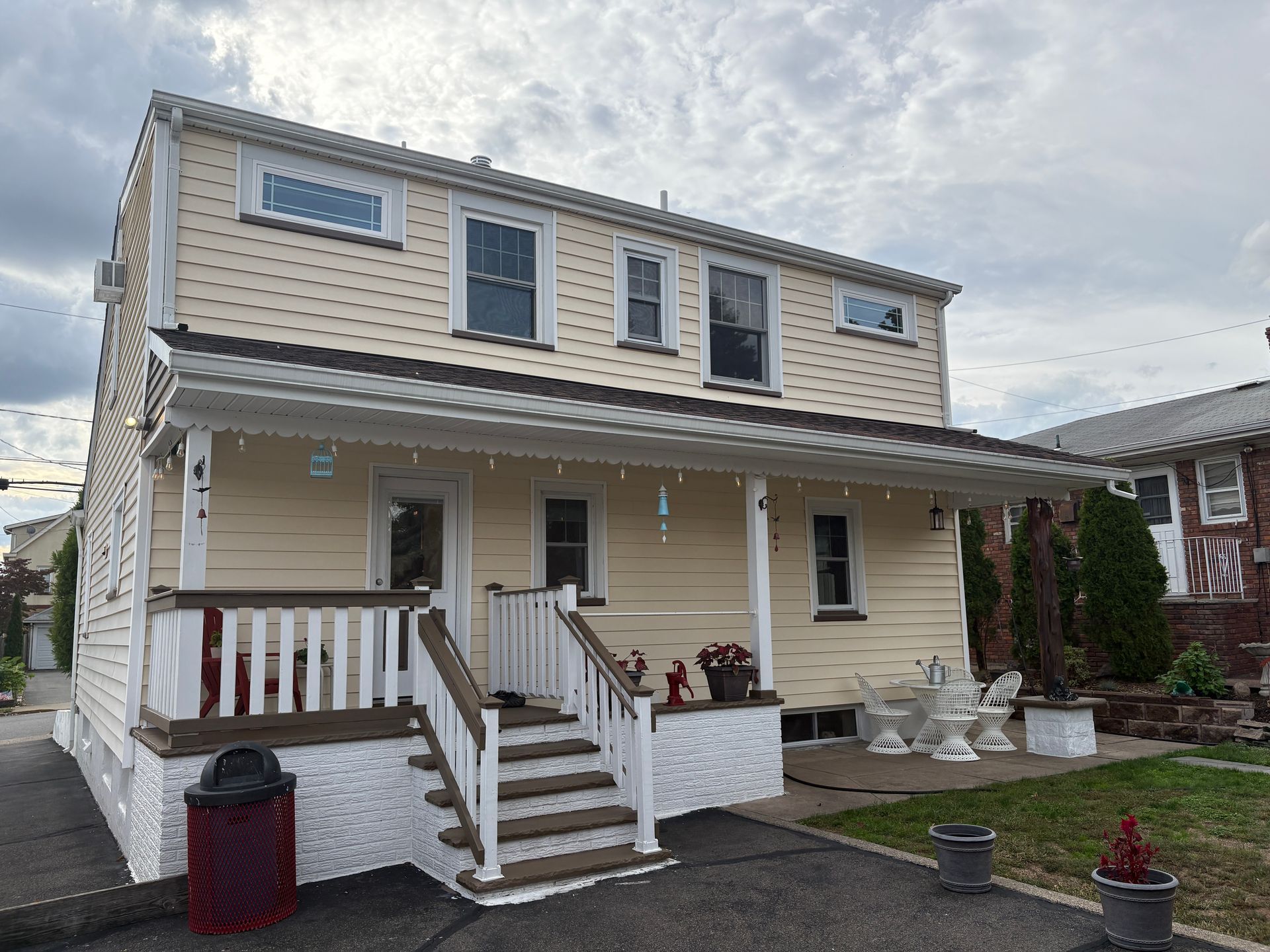 Two-story beige house with a porch. White trim, steps, and railings. Asphalt driveway and cloudy sky.