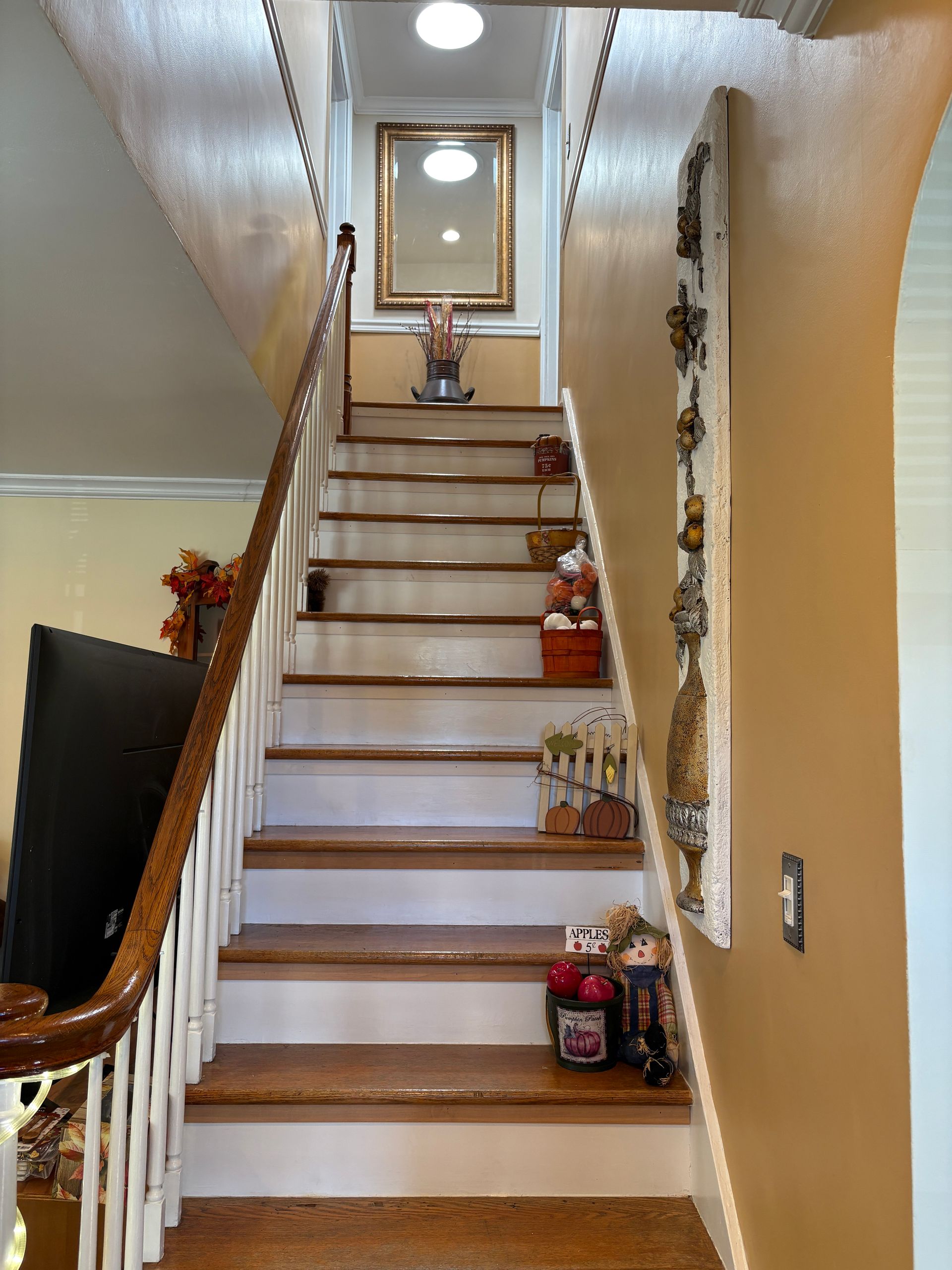 Wooden staircase with white risers, brown treads, ascending towards a mirror on the wall. Fall decor.