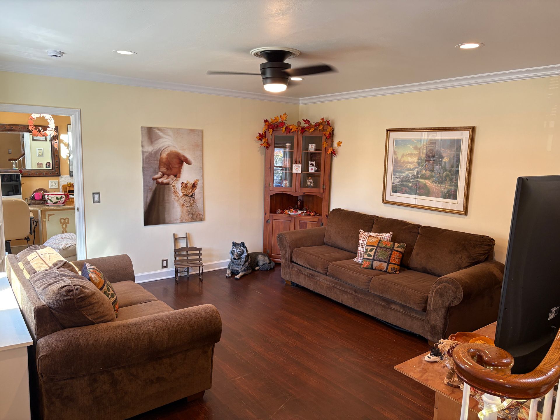 Living room with two brown couches, artwork, and corner cabinet; dark wood floor, light yellow walls.