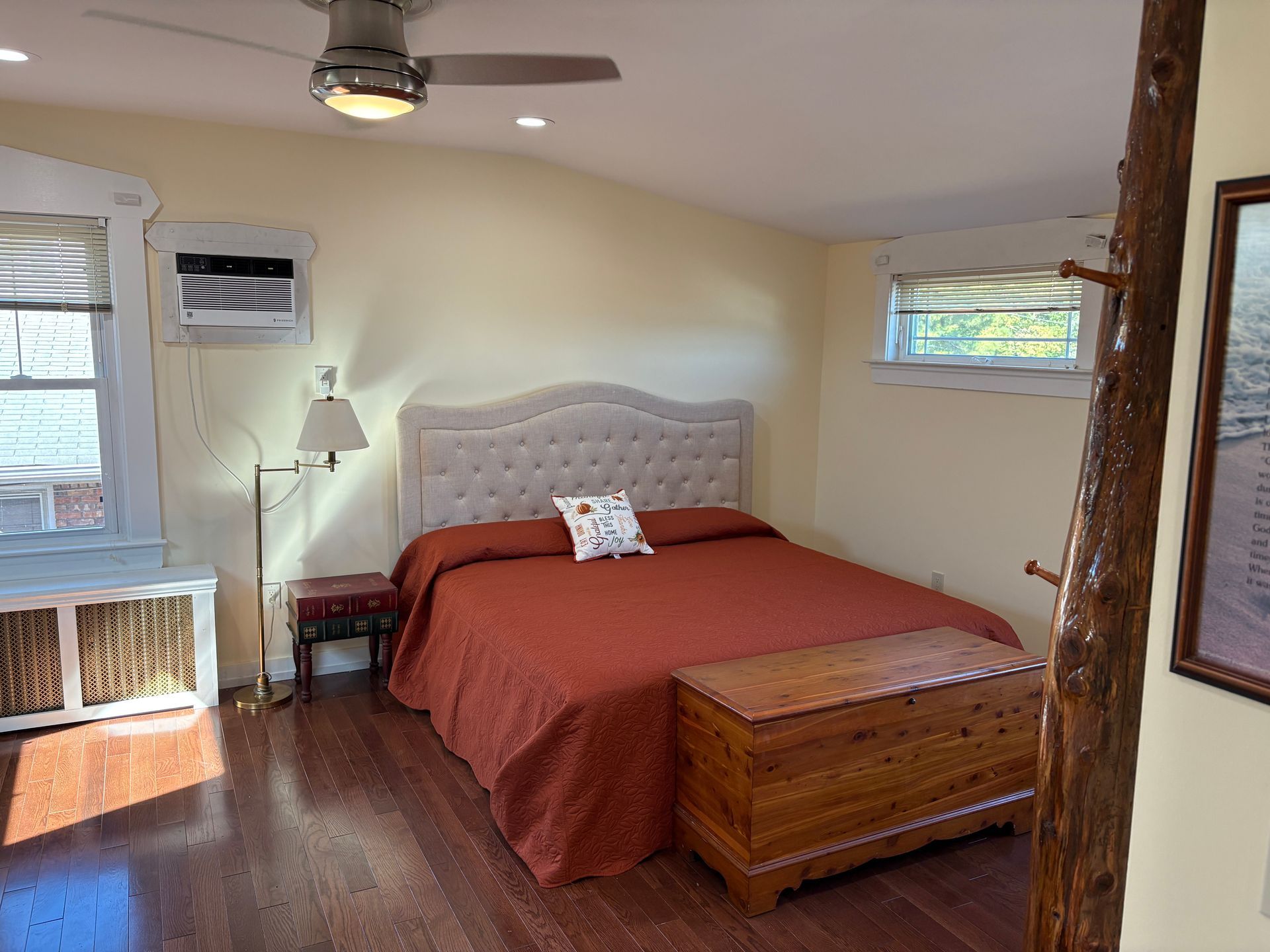 Bedroom with bed, trunk, wooden floor, windows, and a coat rack.