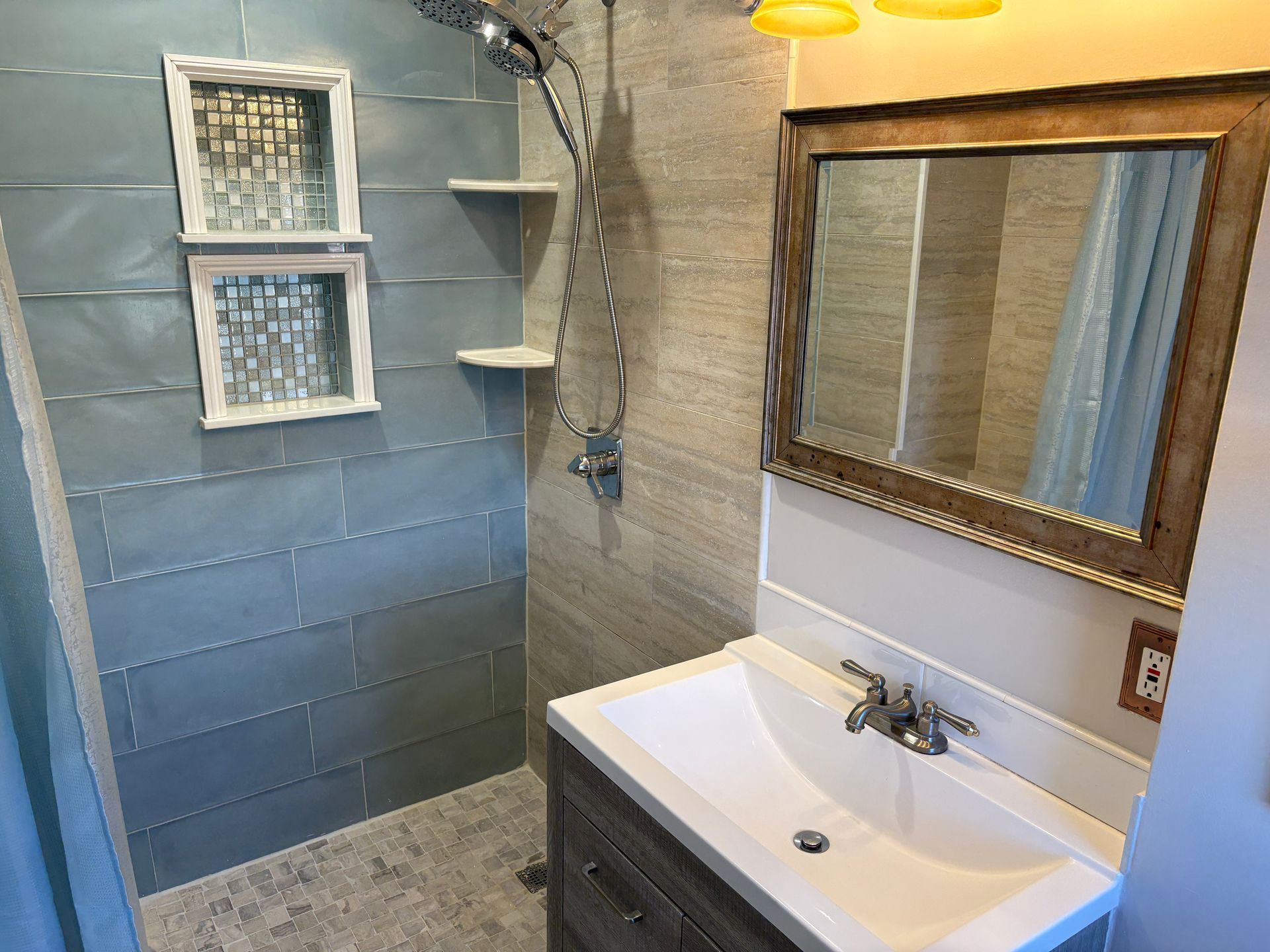 Bathroom with blue tiled shower, vanity with sink, and framed mirror.