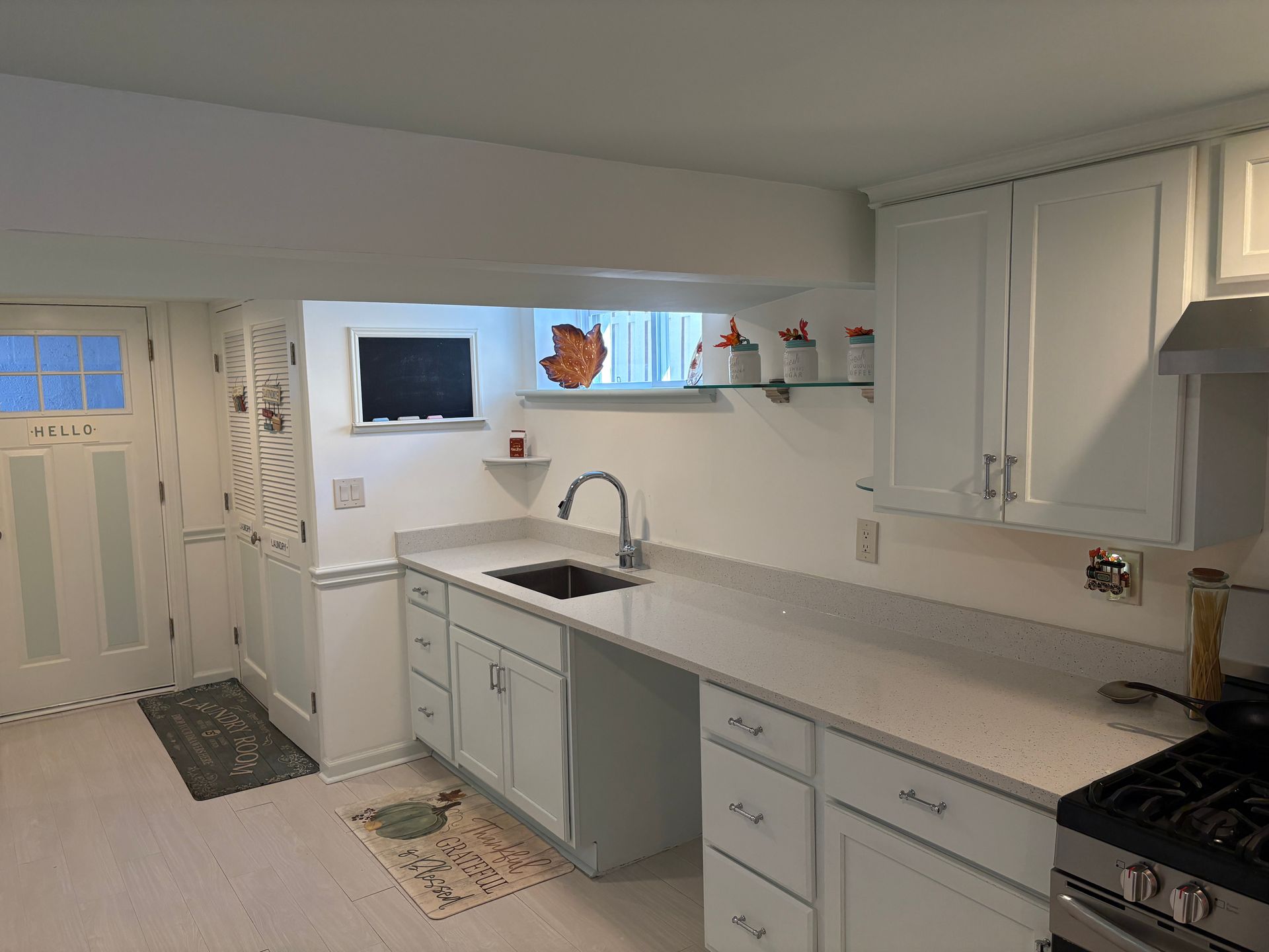 White kitchen with countertop, cabinets, sink, window, stove, and a decorative chicken.