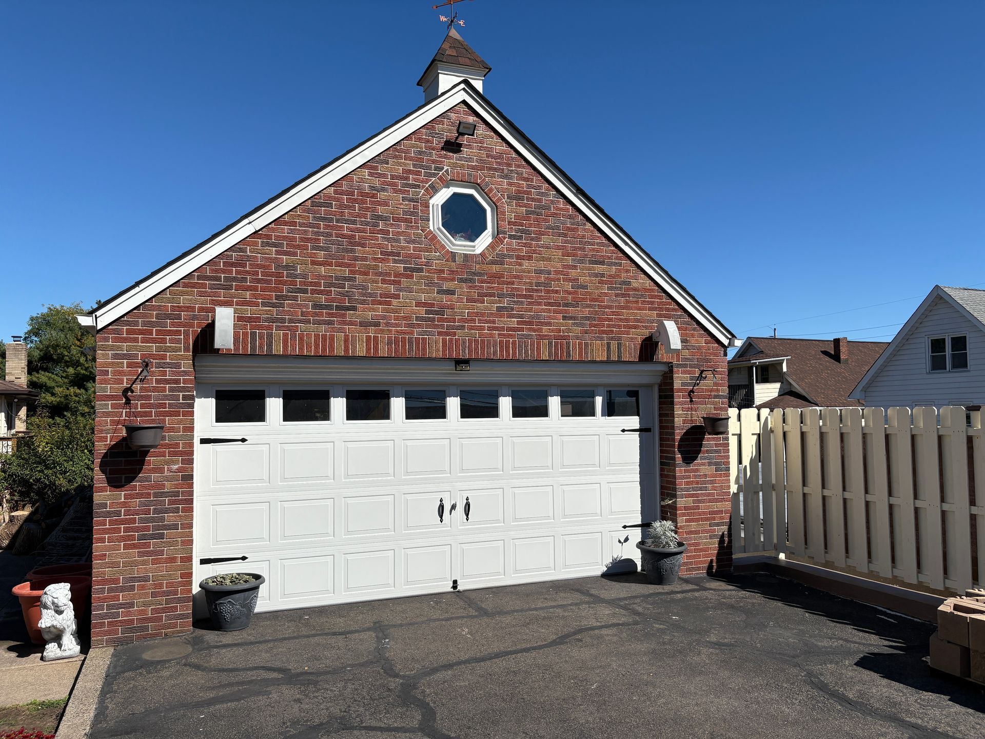 Brick garage with white garage door, small round window, and asphalt driveway.