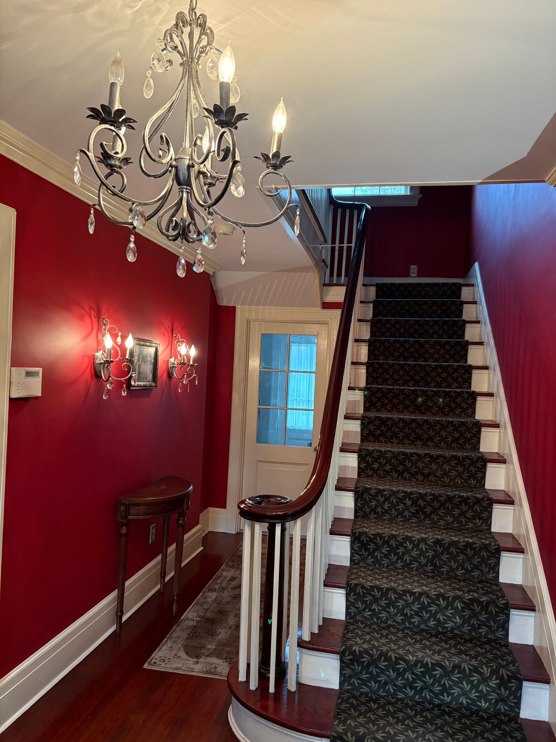 A hallway with red walls, staircase, and chandelier.