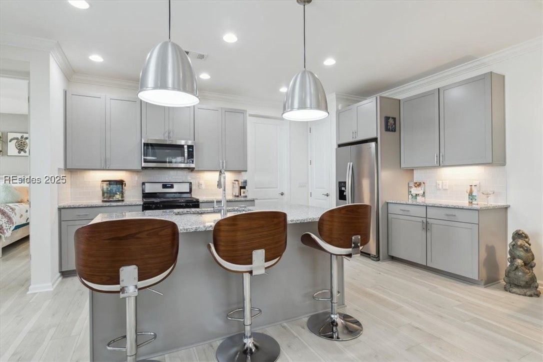 Modern kitchen with gray cabinets, stainless steel appliances, island with brown bar stools, and pendant lights.