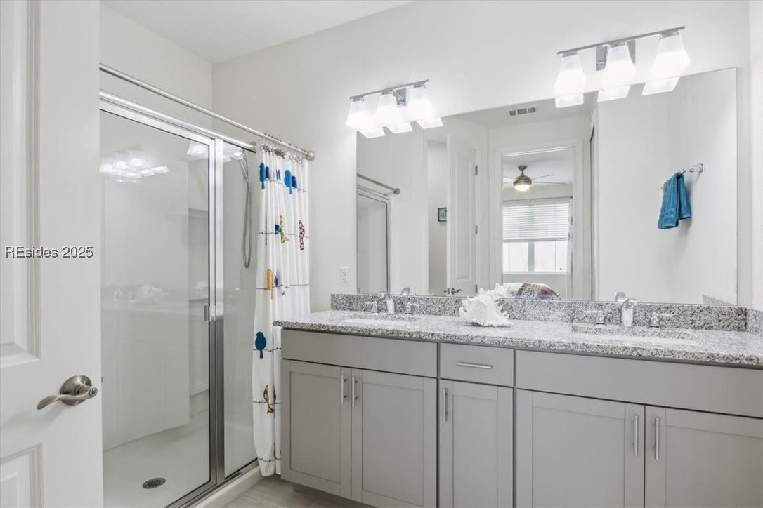 Bathroom with a glass shower, double vanity, grey cabinets, and light grey countertop.